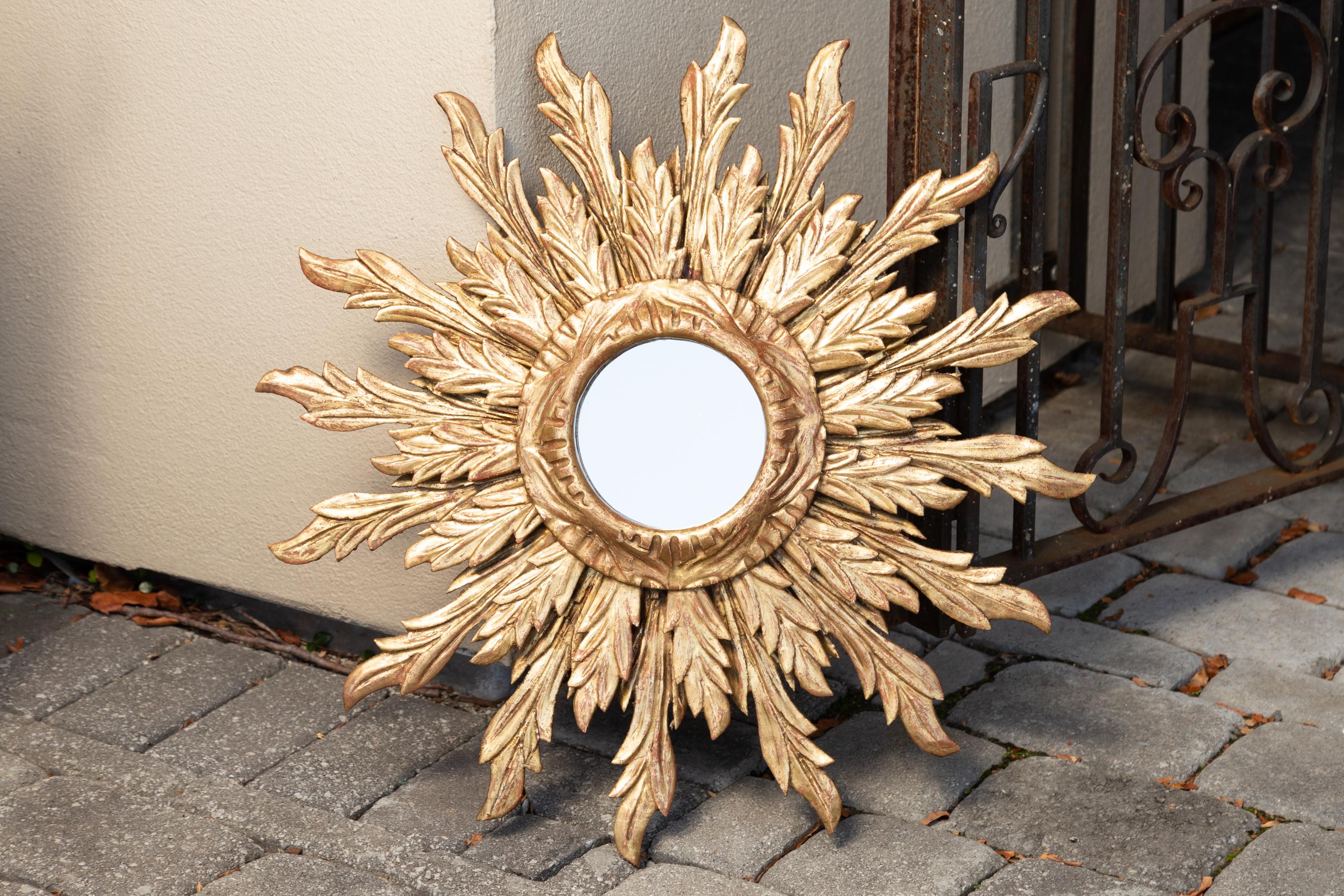 A French giltwood double layered sunburst mirror from the mid-20th century, with wavy sunrays. Born in France during the midcentury period, this exquisite vintage piece features a small size round mirror plate framed by a carved giltwood molding. On