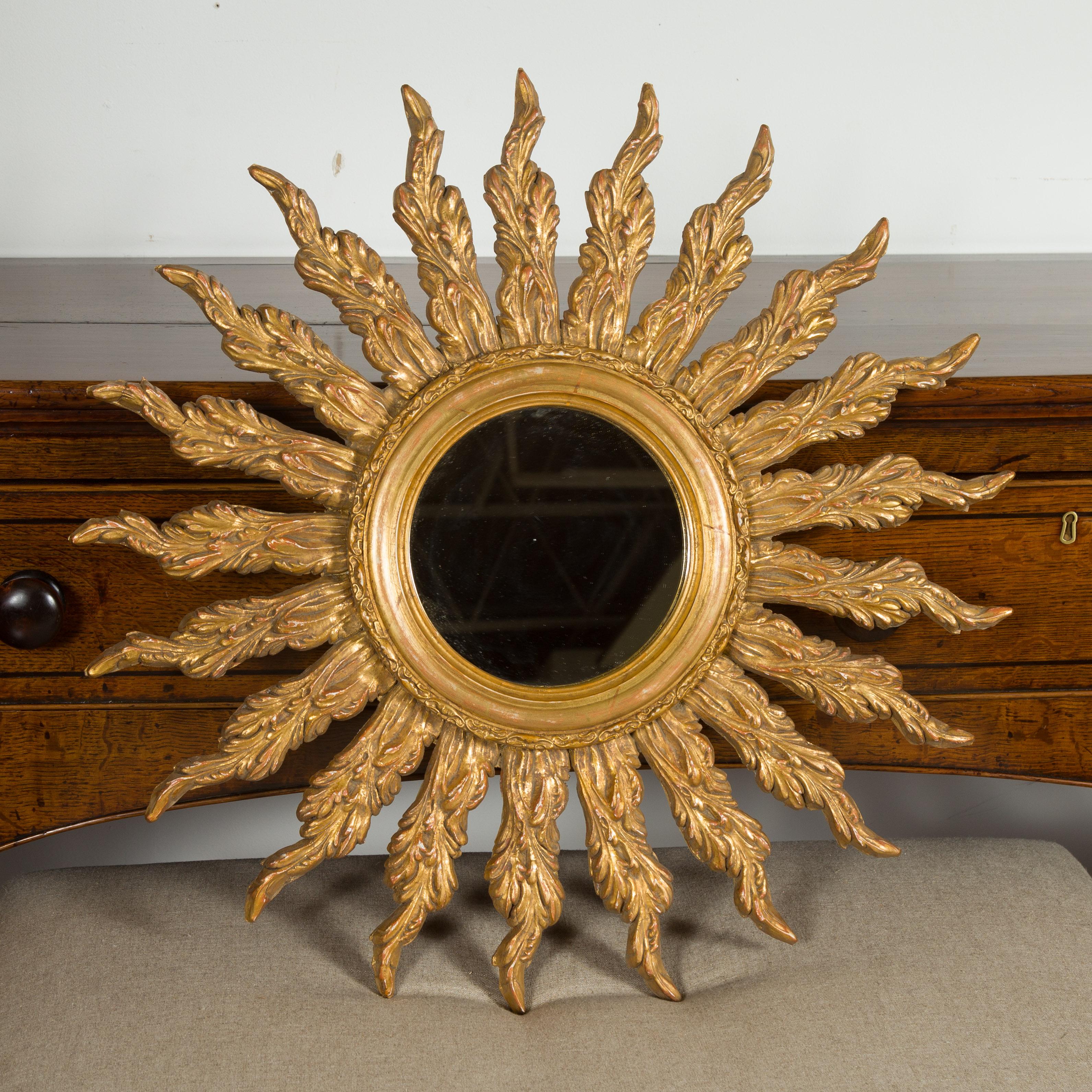 A French giltwood sunburst mirror from the mid-20th century, with wavy sunrays. Created in France during the midcentury period, this vintage piece features a round mirror plate framed by a carved giltwood molding. On the surround, a decor of wavy