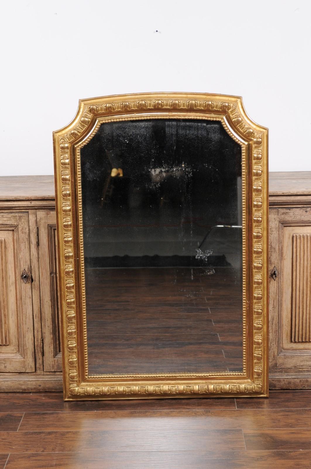 A French giltwood wall mirror from the early 20th century, with carved frame and beaded motifs. Born in France during the early years of the 20th century, this exquisite giltwood mirror features a rectangular silhouette, topped with curving sides.