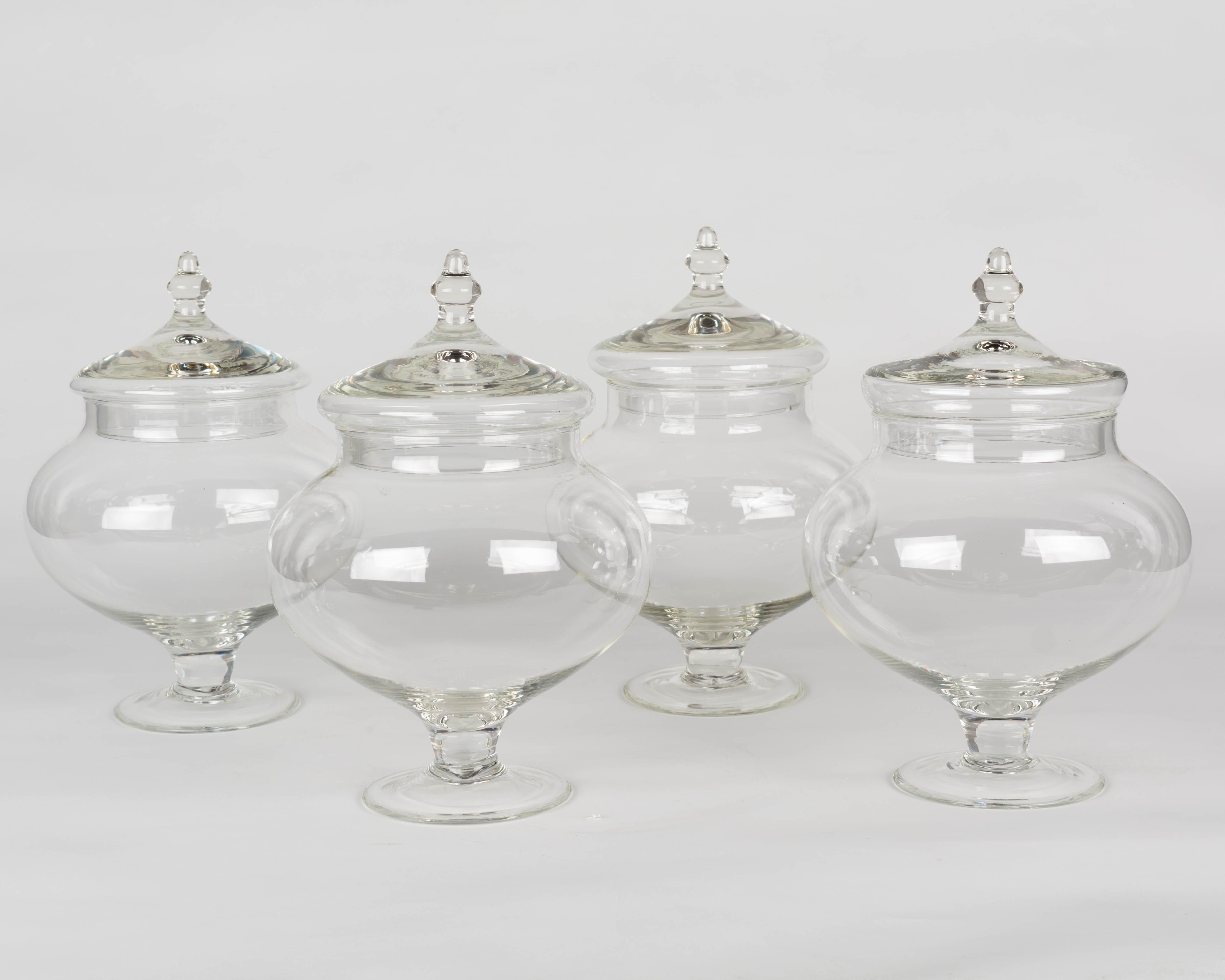 A set of four French blown glass lidded apothecary or candy jars. Smooth form with pedestal base and decorative knob on lid. Light weight, perfect for jelly beans or for use as bathroom canister. Purchased from a confiserie, or sweet shop, along
