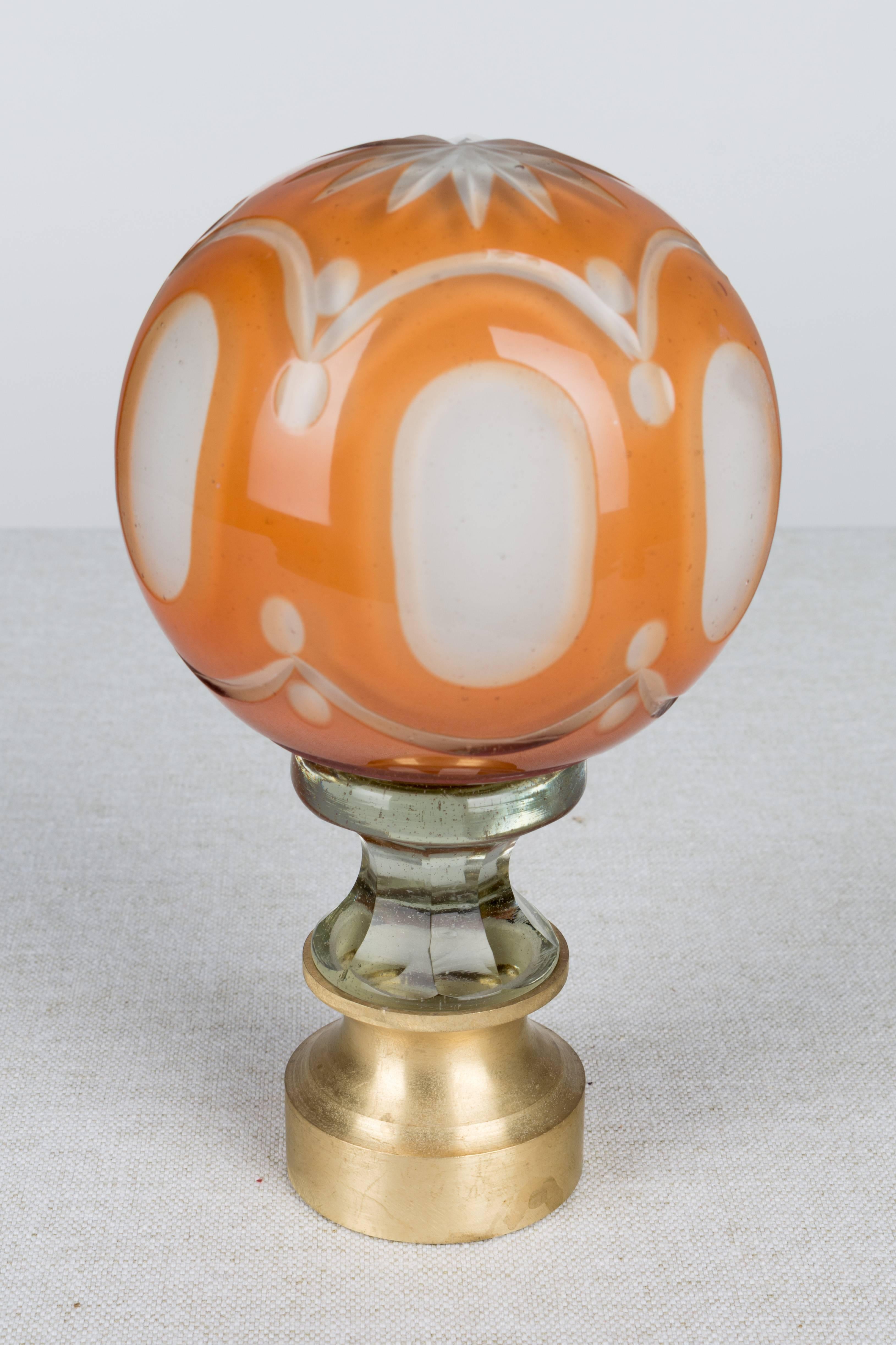 An early 20th Century French glass newel post finial or boule d'escalier. Made of two layers of cased glass with the orange glass surface cut back to the white glass underneath. Brass hardware base. These wonderful finials were used as decorative