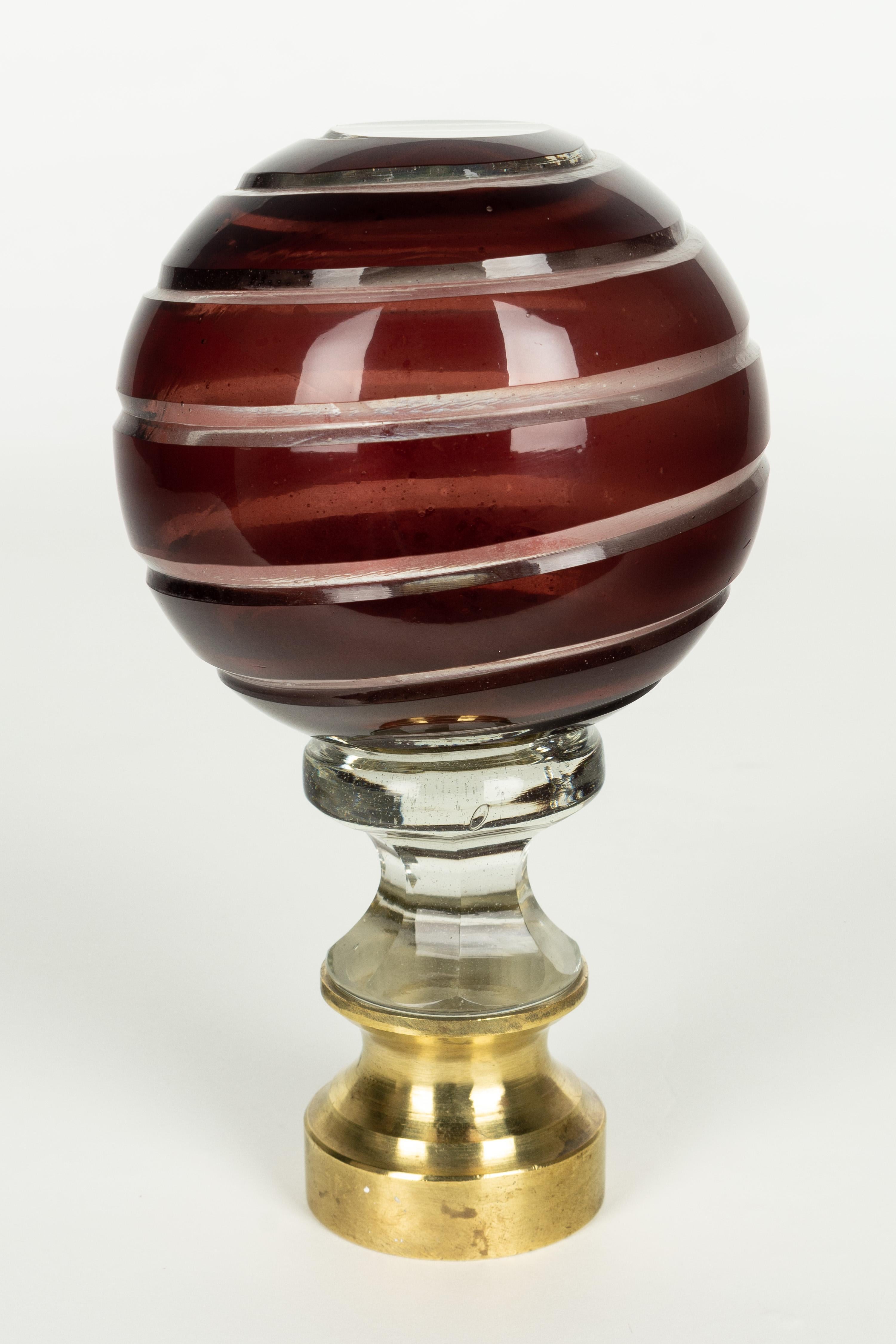 A French crystal newel post finial or boule d'escalier. Made of two layers of cased glass with the ruby red glass surface cut in a spiral pattern revealing clear glass underneath. Brass hardware base. These wonderful finials were used as decorative