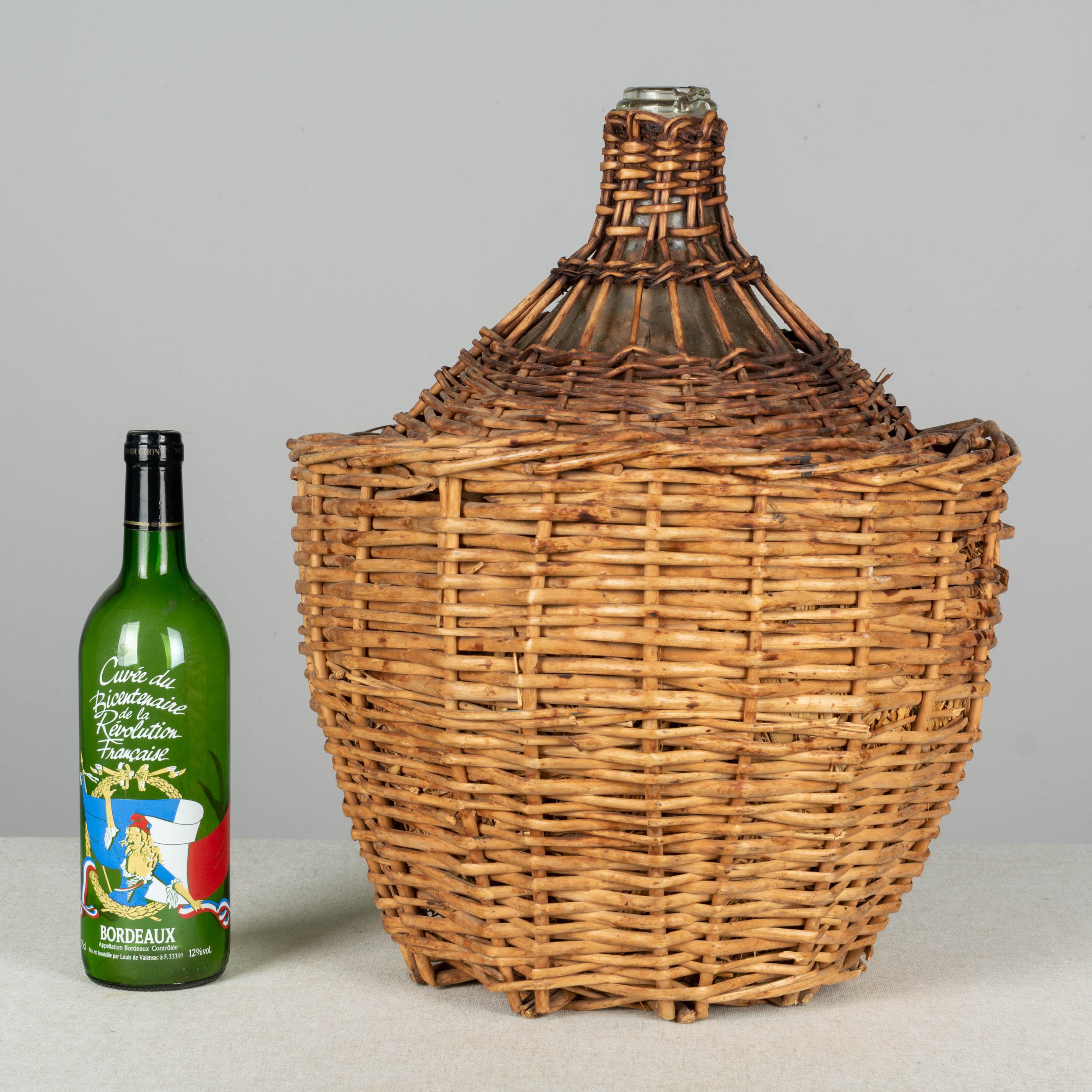 A large French globular form glass dame Jeanne, or demijohn bottle enclosed in a woven wicker basket lined with straw. Small chip to mouth of bottle.