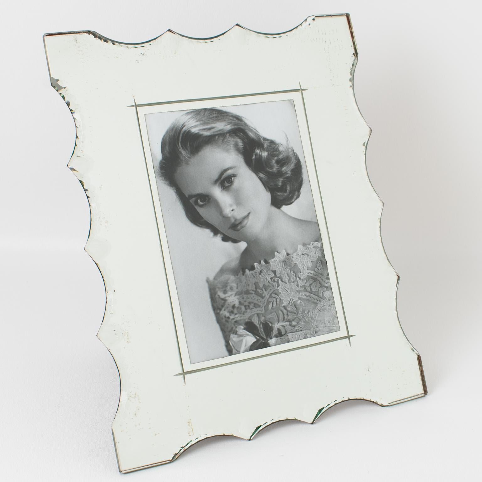 This elegant 1940s French mirrored picture photo frame features an impressive carved shape with geometric bevelling around it. Although of French origin, the design of this frame is close to the glamorous American Hollywood Regency style of the