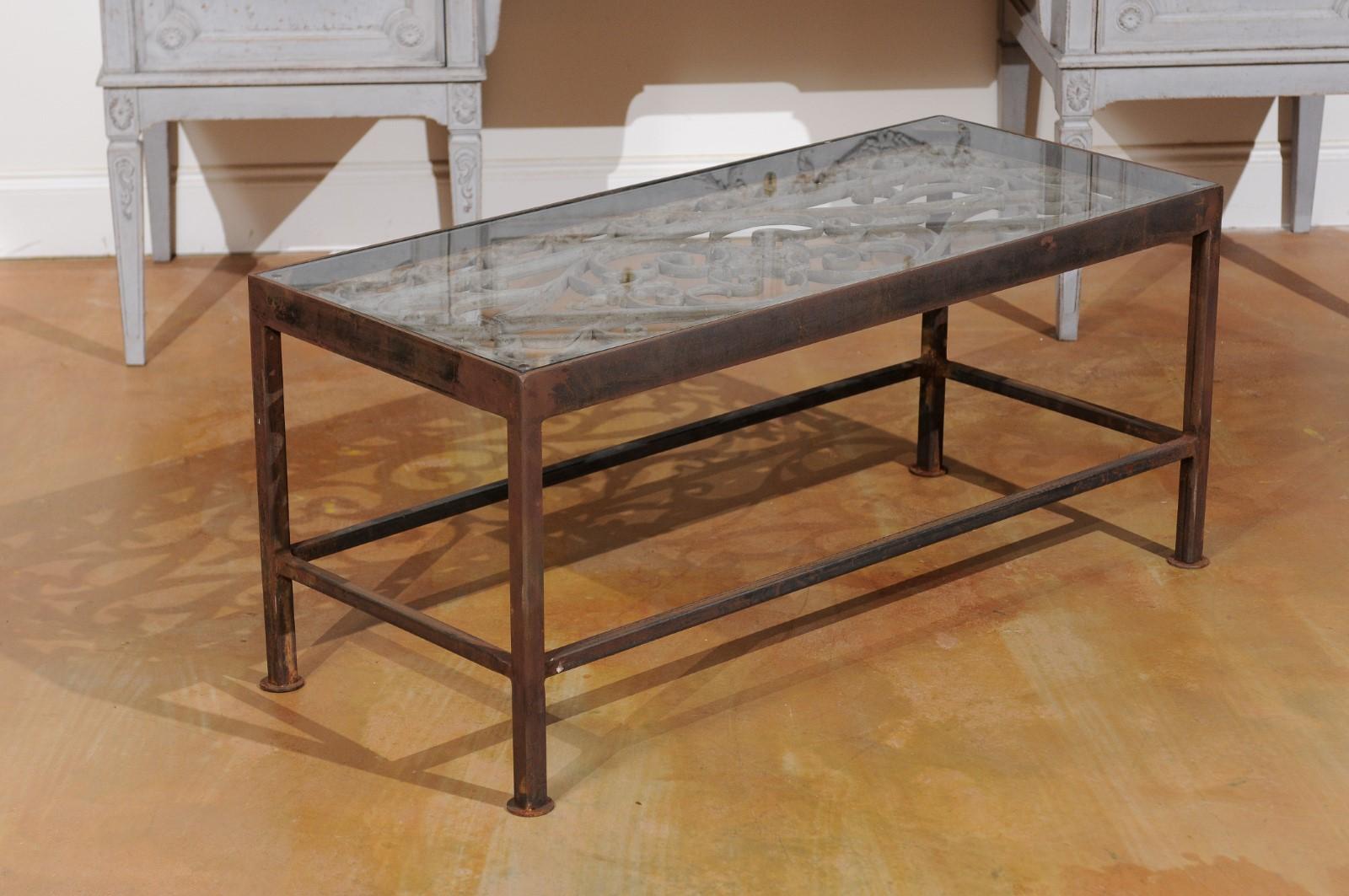 A French 19th century iron balcony made into a coffee table with custom made glass top. Our eye is immediately drawn to the upper section presenting a rectangular glass top sitting above the exquisite metal work from a 19th century French