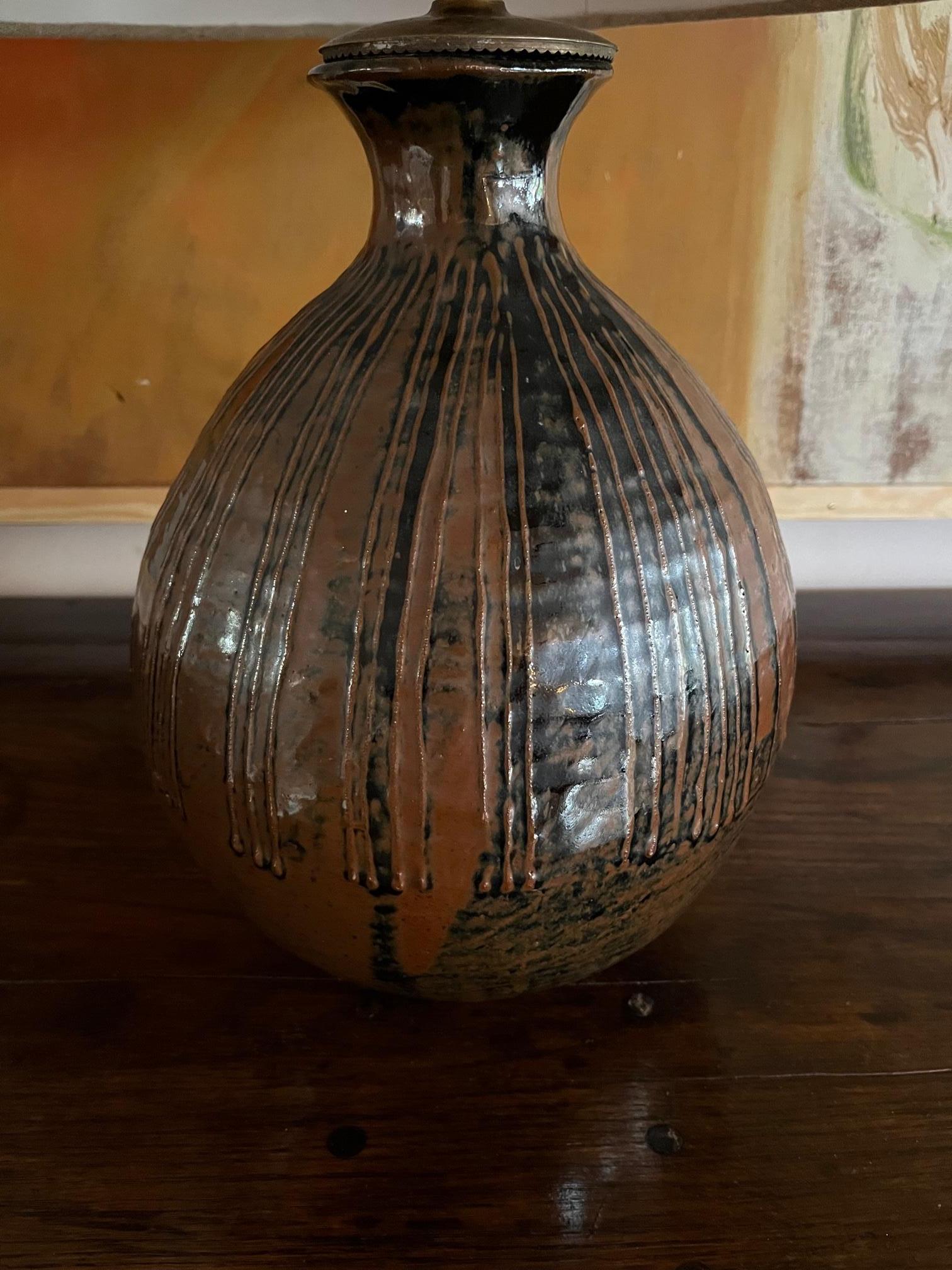 A heavy glazed ceramic, stoneware lamp. Brown with glazed black detail. There is a firing crack to the glaze and also a minor chip to the back of the lamp. This should be visible in one of the photos. The shade is used for display and not included.