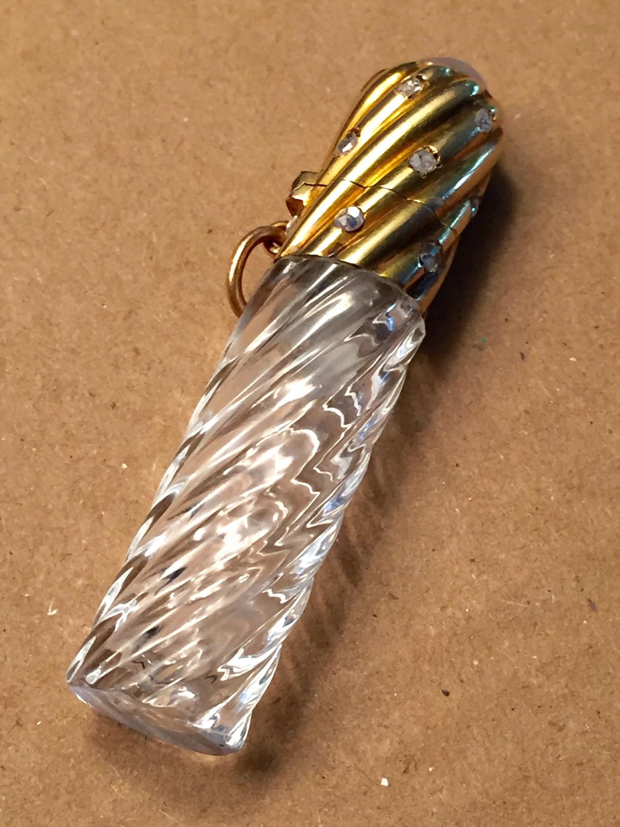 A ribbed crystal bottle is topped by a matching 18k gold ribbed section set with rose cut diamonds and finished with a star sapphire on top. There is a stopper inside and a loop on one side to use if you want to suspend the vial from a gold chain or