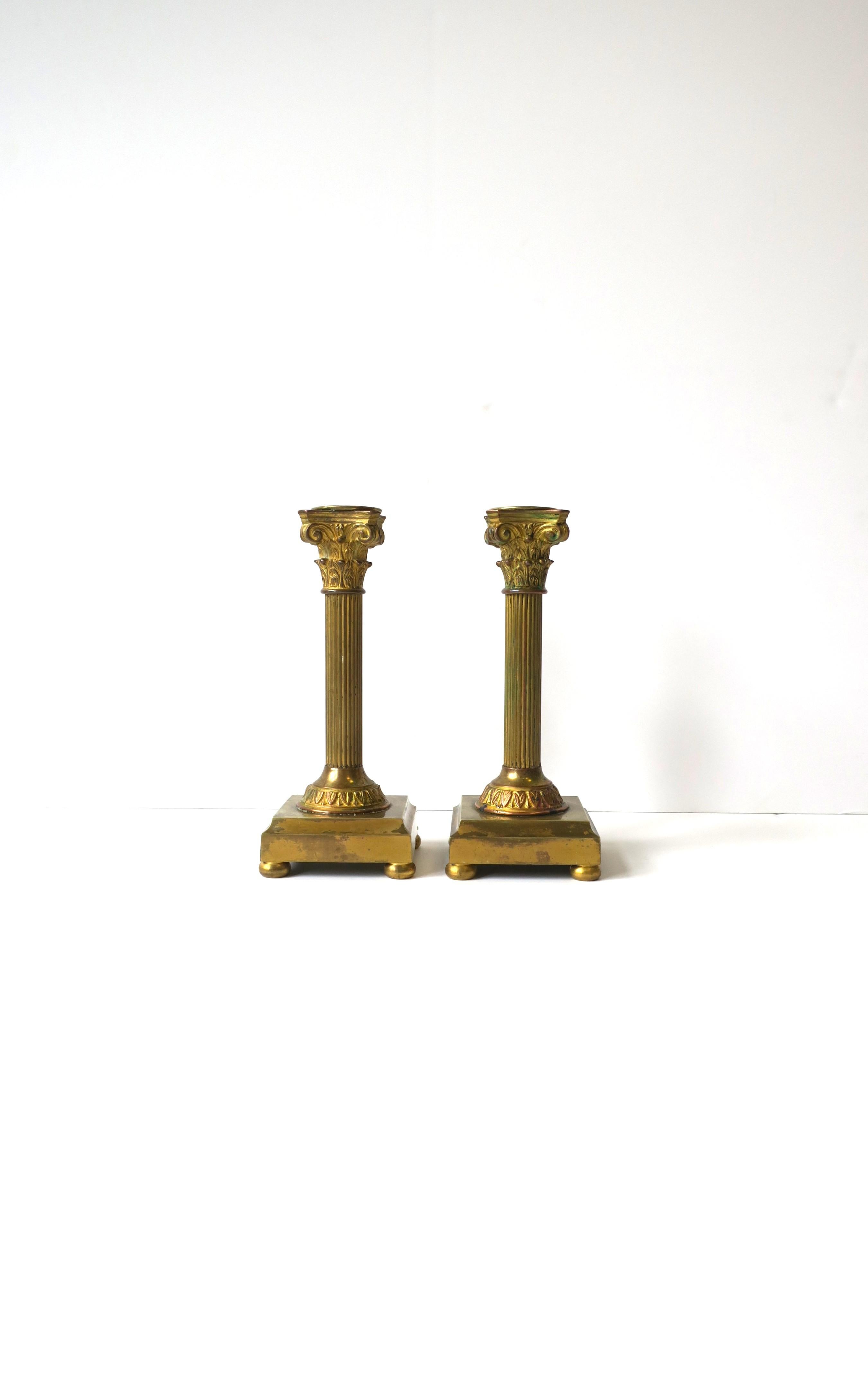 A substantial pair of French gilt bronze Corinthian column candlestick holders in the Neoclassical style, circa late-19th century, France. Candlesticks depict the Corinthian column, made of bronze with a copper, brass and gold gilt overlay, square