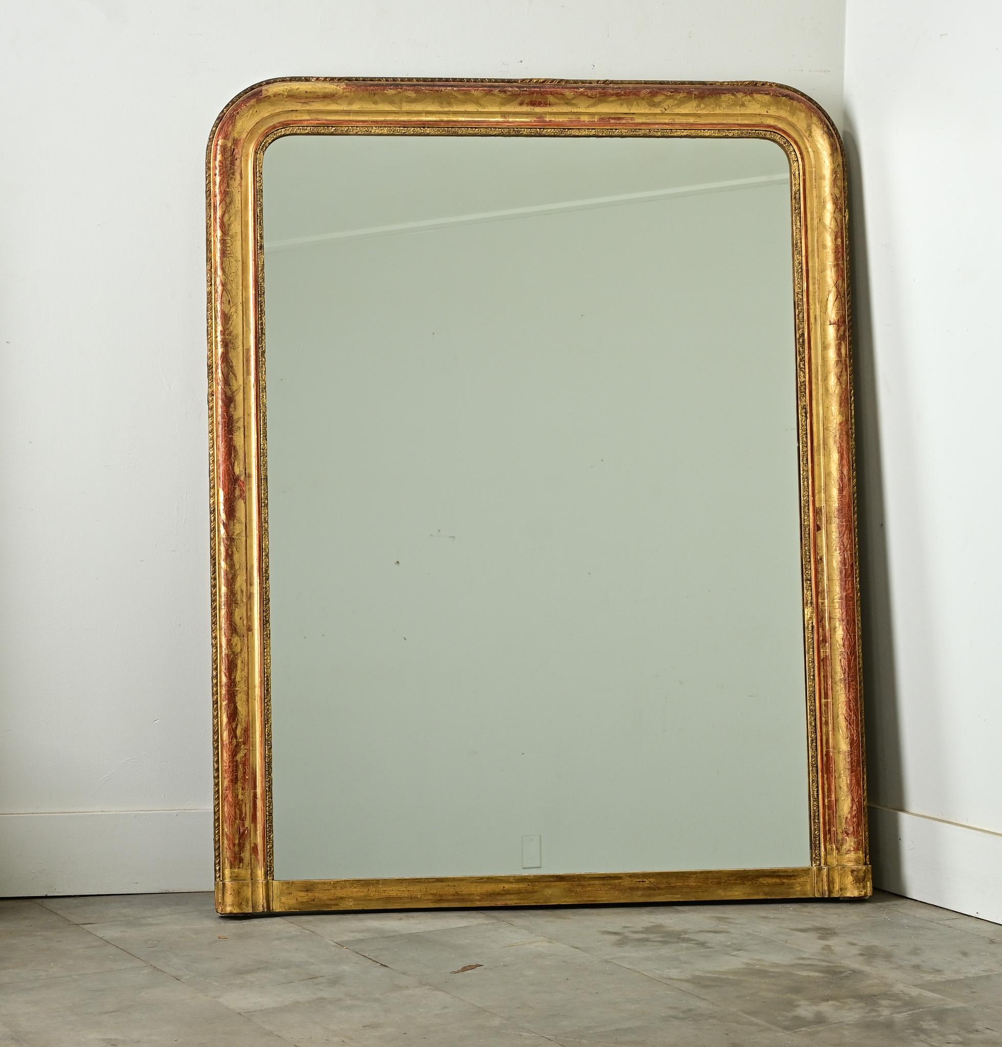 A graceful floral motif of iris traces the frame of this gilt Louis Philippe mirror, brought to life by the red bole coming through the gold leaf, visual imagery likely brought back from French colonies around Southeast Asia. While a ribbon-twist