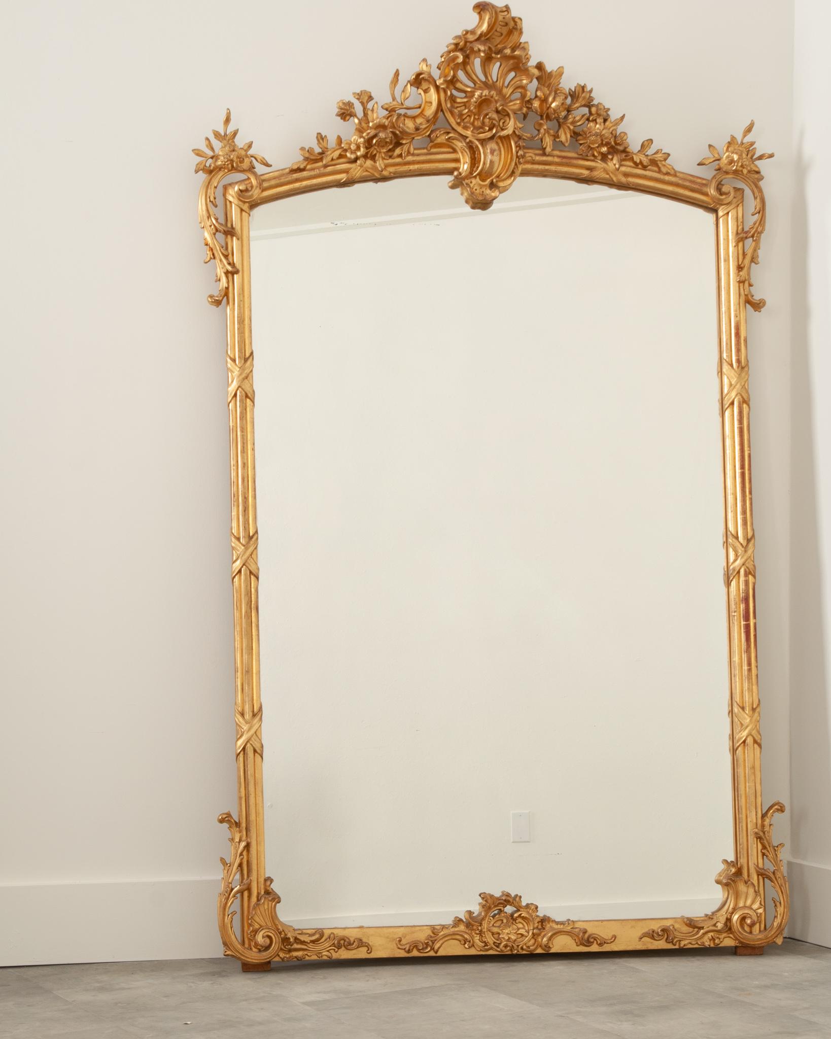 A stunning French mantle mirror covered in carved details and its original water gilding finish. At the top of this Louis XV style mirror is the iconic C scroll of Rococo design surrounded in floral carvings that dance beyond the frame of the