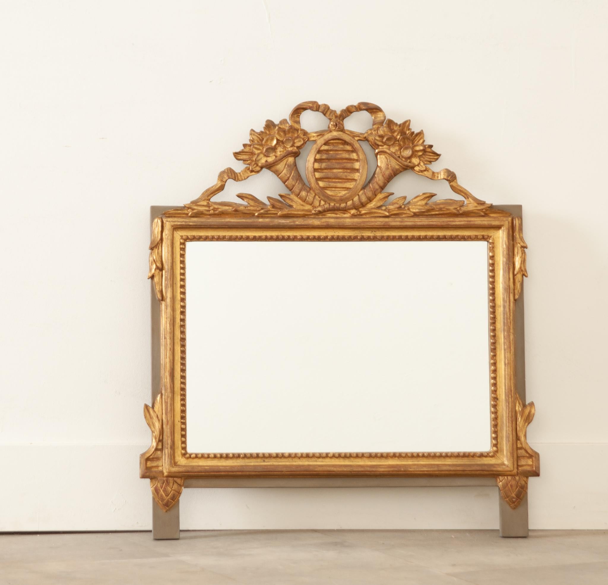 A darling gold gilt Louis XVI style pier mirror from France, crafted during the 1870s. A carved crest of flower bouquets and bowed ribbon sits atop the frame and has its original brilliant wanter guild finish. The mirror frame is surrounded by a