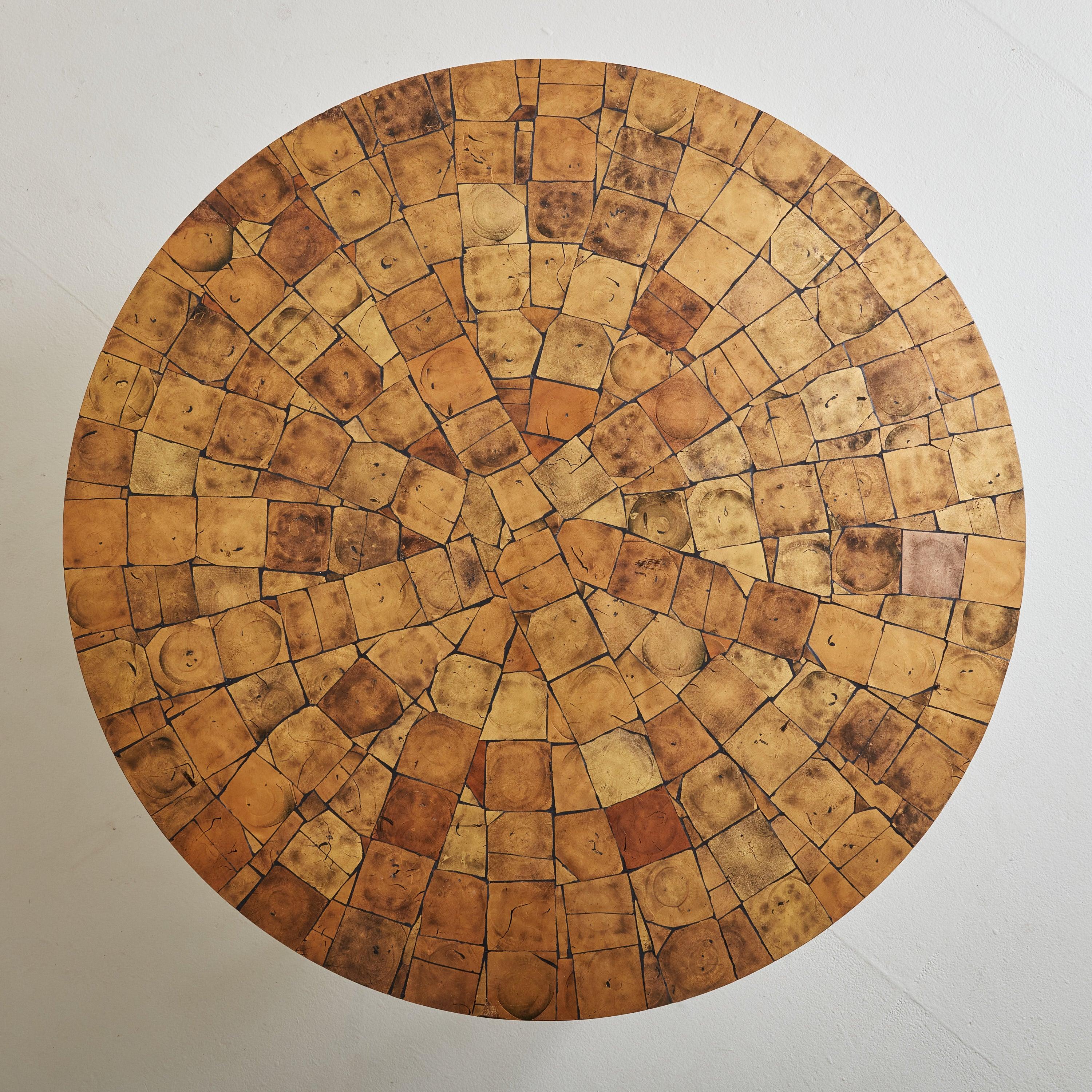 Une table basse parisienne des années 1970 qui fusionne l'artisanat et la forme moderniste. Le plateau de verre est méticuleusement incrusté de feuilles d'or appliquées à la main, créant une mosaïque de chaleur et de texture. Ancrée par un piédestal