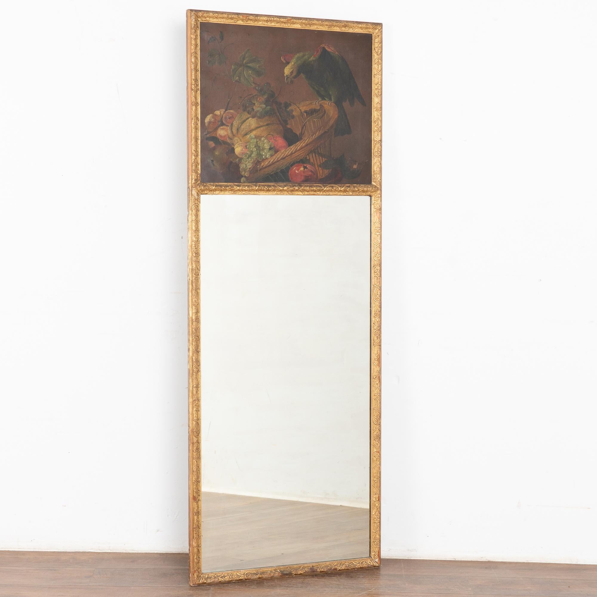 Joli miroir trumeau avec la partie supérieure peinte à l'huile sur toile avec des fruits et des courges dans un panier et un perroquet perché sur le bord. 
D'une hauteur d'un peu moins de 6 pieds, il constitue un ajout spectaculaire, quel que soit