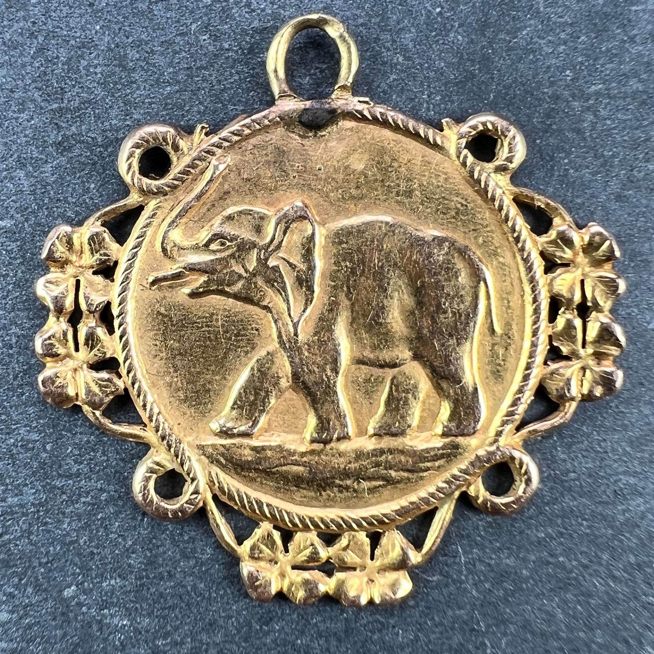 Un ciondolo francese in oro giallo 18 carati (18K) disegnato come una medaglia che raffigura un elefante portafortuna con la proboscide sollevata all'interno di una cornice in corda che incorpora trifogli o quadrifogli per rappresentare la buona