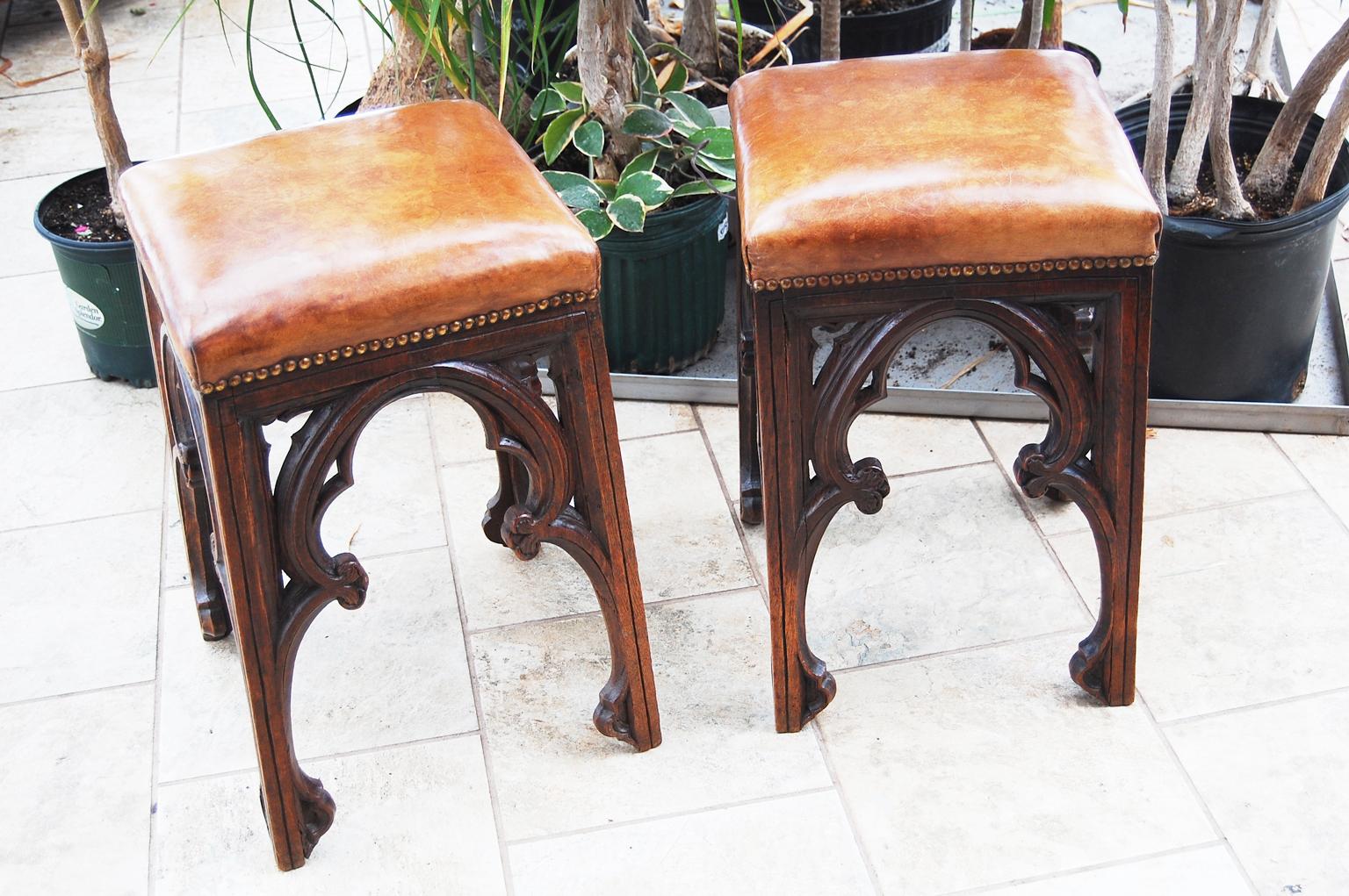 French 19th century gothic revival pair of stools in oak.  These beautifully carved stools have gothic carved molded arches on all four sides; the legs are slightly splayed which makes for excellent stability and the seats are hand dyed leather. 
