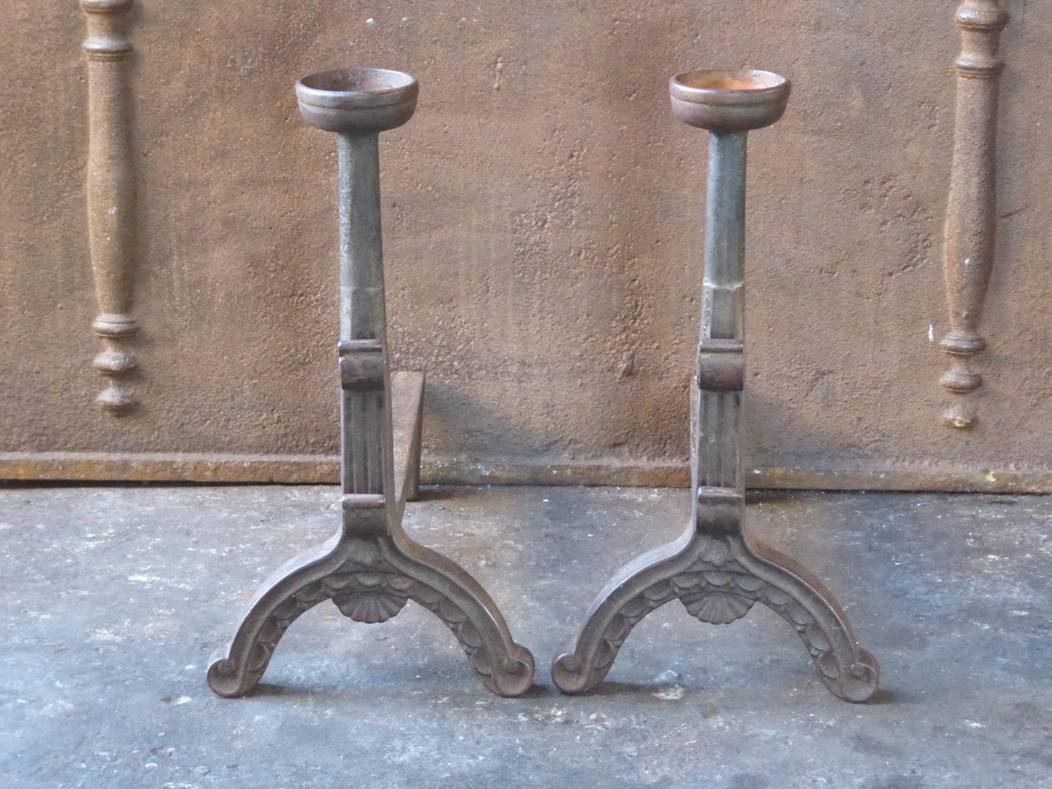 19th-20th century French andirons made of cast iron. The style of the andirons is Gothic. The andirons have spit hooks to grill food and a cup to keep drinks warm. They are in a good condition.