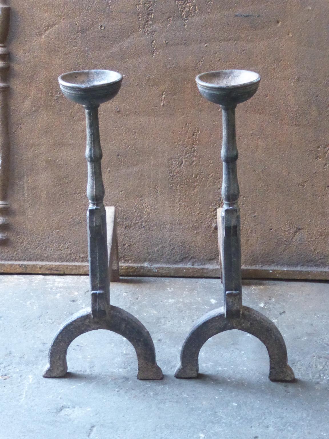 20th century French andirons made of cast iron. The style of the andirons is Gothic. The andirons have spit hooks to grill food and a cup to keep drinks warm. They are in a good condition.