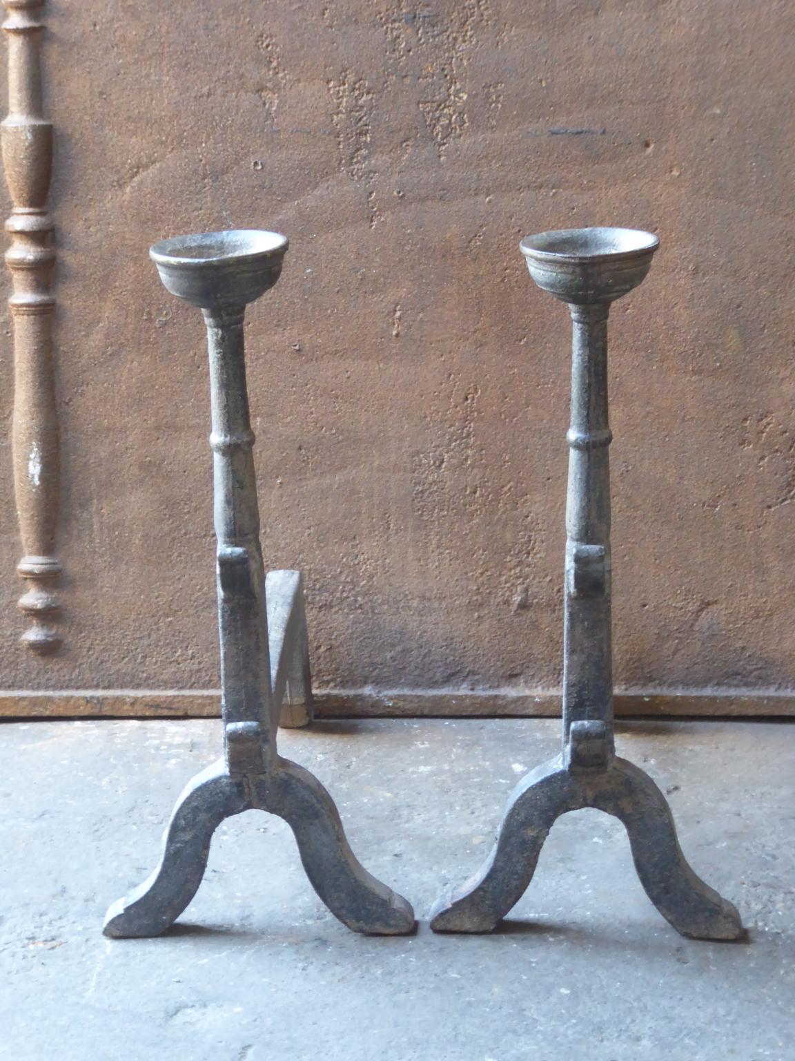 20th century French andirons made of cast iron. The style of the andirons is Gothic. The andirons have spit hooks to grill food and a cup to keep drinks warm. They are in a good condition.