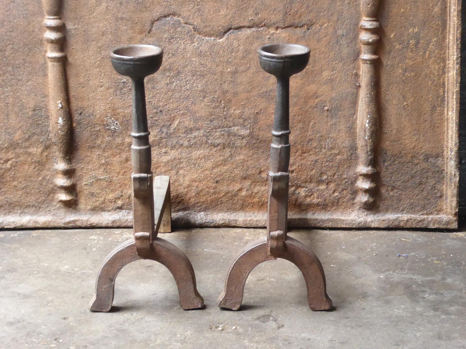 20th century French andirons made of cast iron. The style of the andirons is Gothic. The andirons have spit hooks to grill food and a cup to keep drinks warm. They are in a good condition.