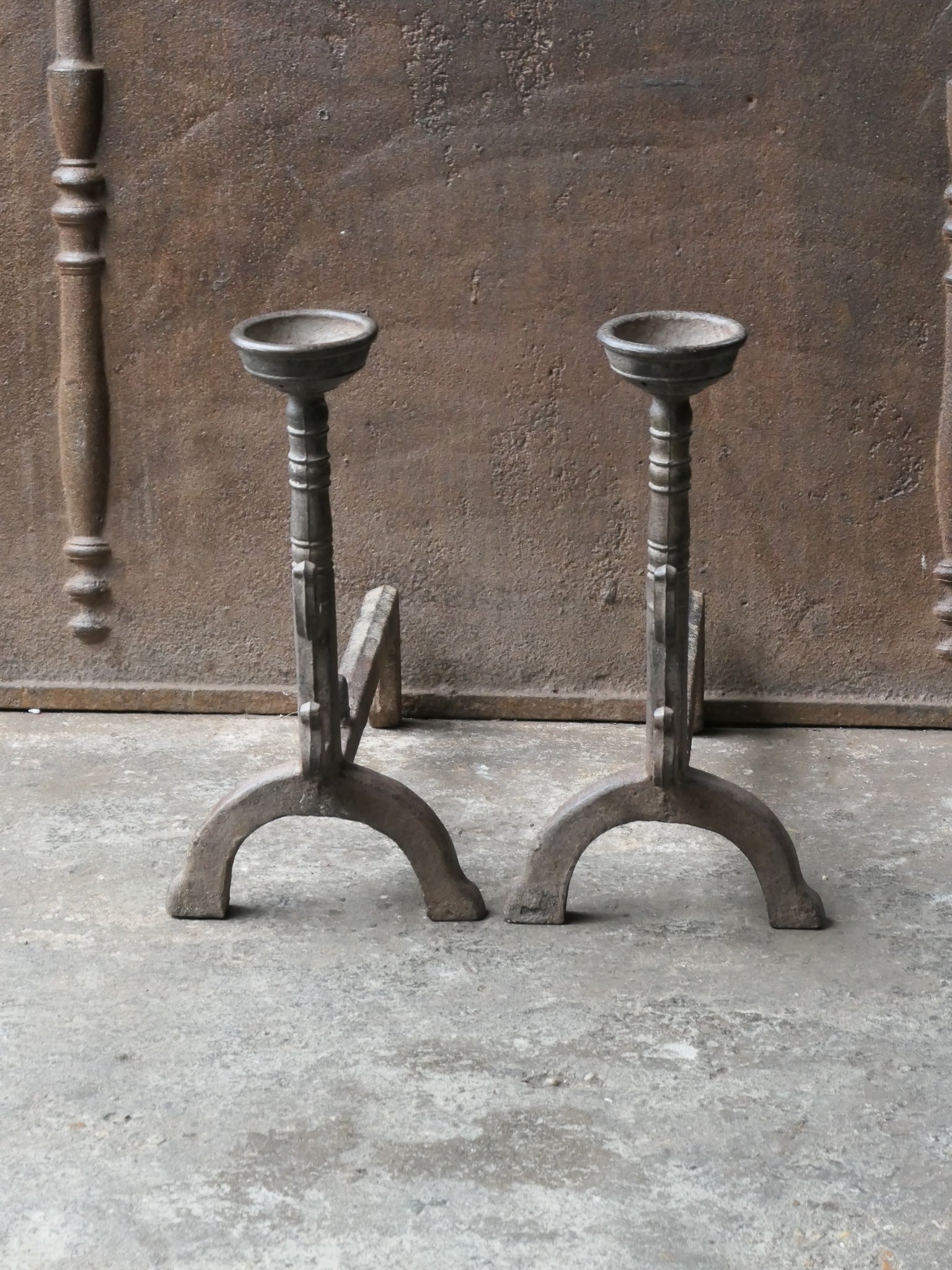 20th century French andirons made of cast iron. The style of the andirons is Gothic. The andirons have spit hooks to grill food and a cup to keep drinks warm. They are in a good condition.