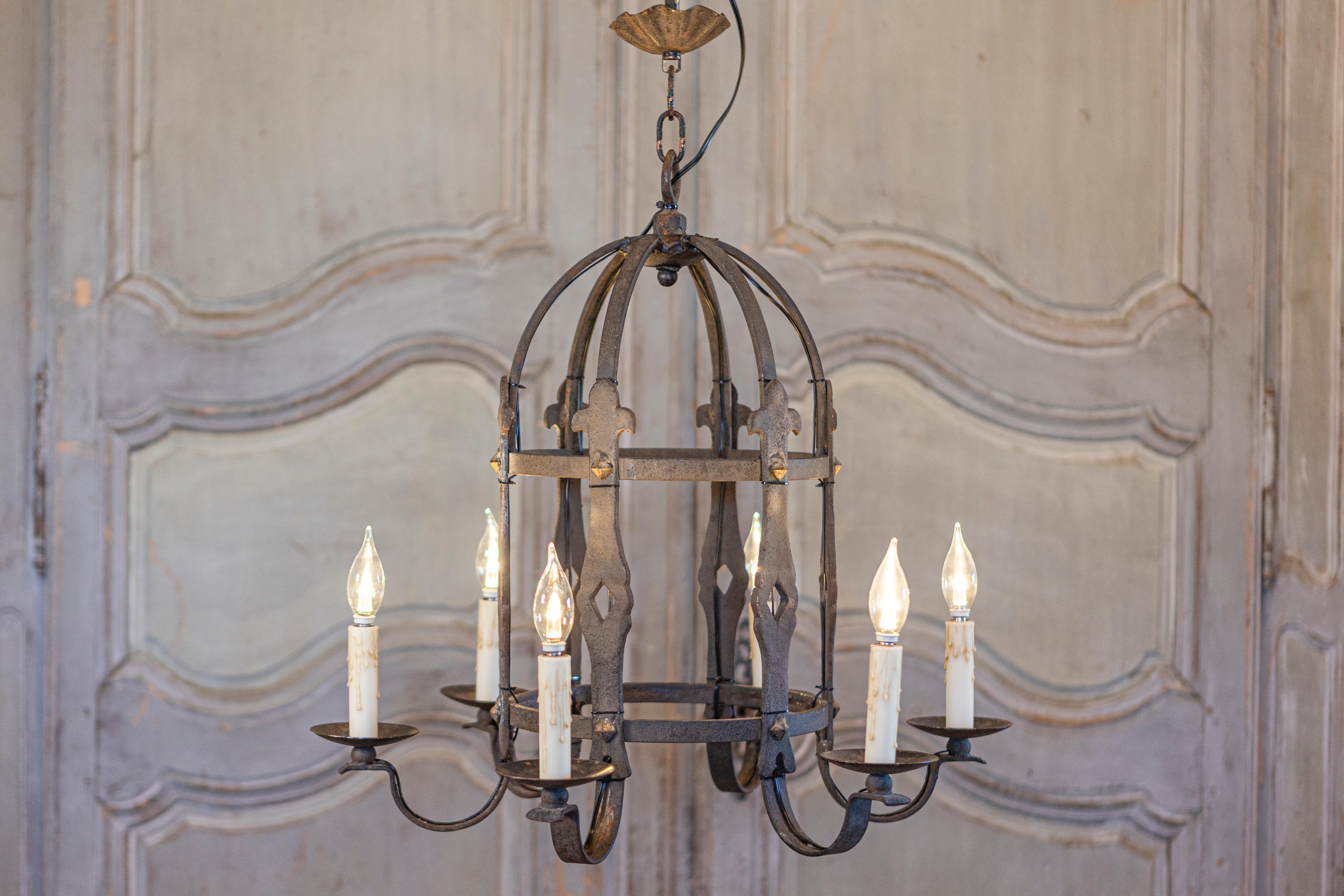 A French Gothic style cage shaped wrought iron chandelier from circa 1950 with six scrolling arms. This French Gothic style chandelier from circa 1950 is masterfully crafted from wrought iron, featuring a cage-like silhouette with six elegantly