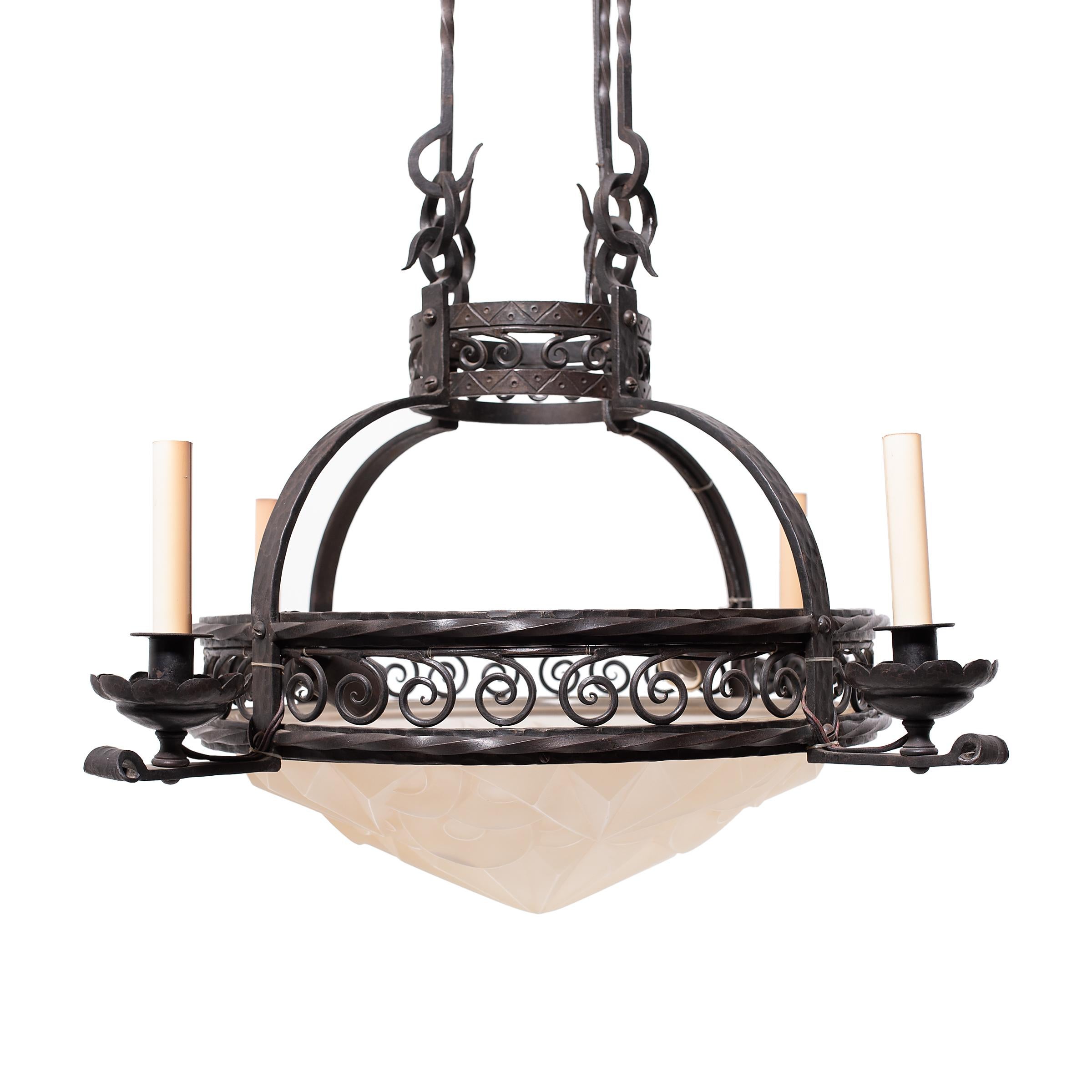 This magnificent frosted glass chandelier combines the soft finish of molded Art Deco glass with the striking forms of a Gothic wrought iron frame. The central domed glass bowl is molded with stylized geometric patterns and sits within a round frame