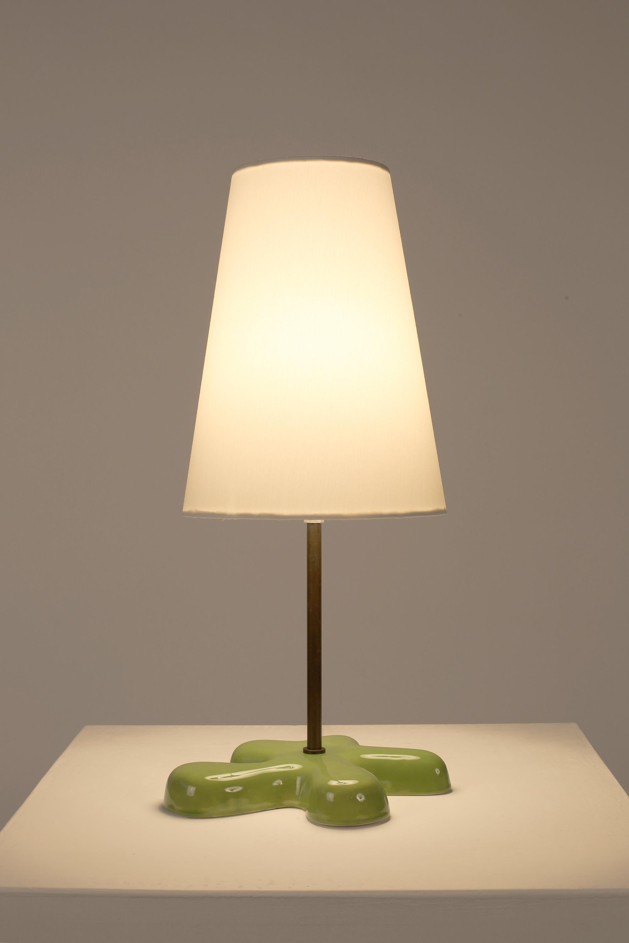 Une lampe de table amusante et postmoderne en laiton patiné avec une base fluide et libre en céramique émaillée verte. France, fin du 20e siècle. Livrée avec un abat-jour conique en coton blanc sur mesure.