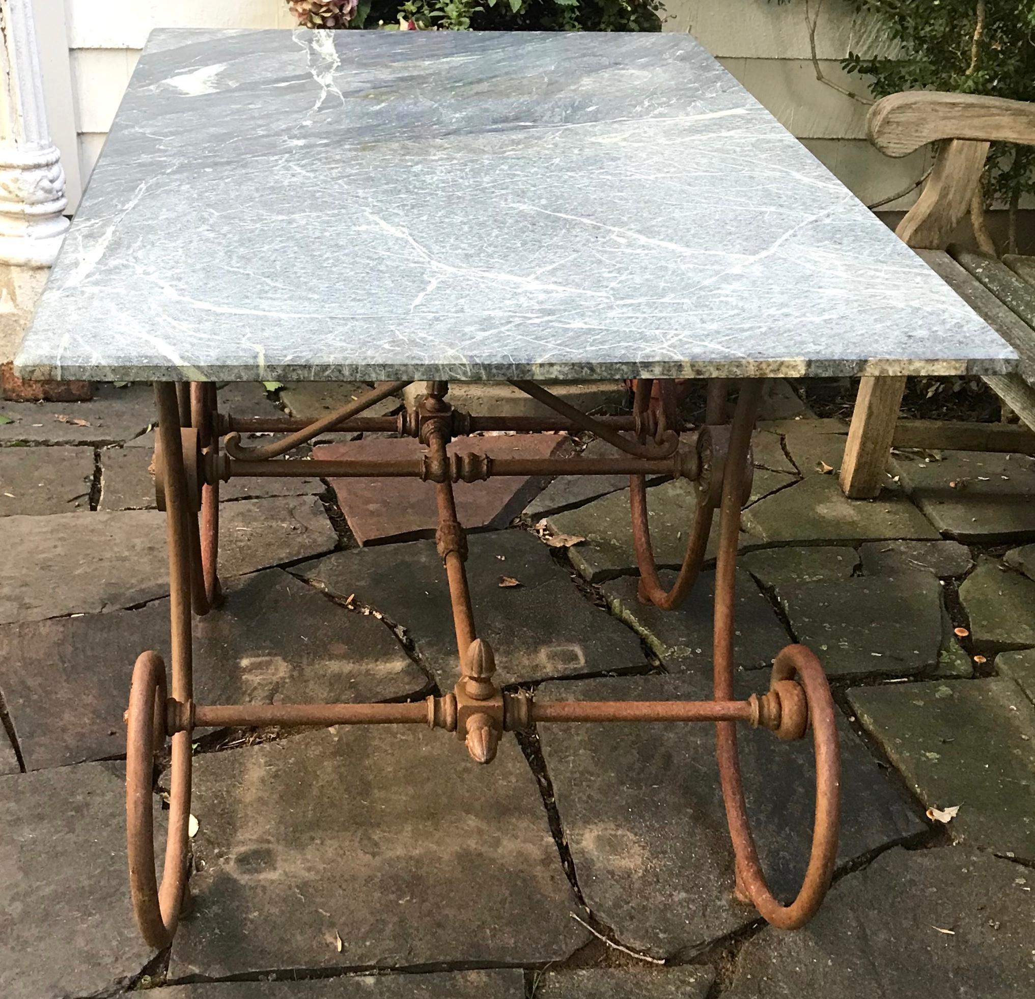 French green marble top baker's table. 19th century scrolling metal trestle form base with center medallions and acorn stretcher finials all supporting a rich green slab of French marble. Wear commensurate with use; base has a uniform distress