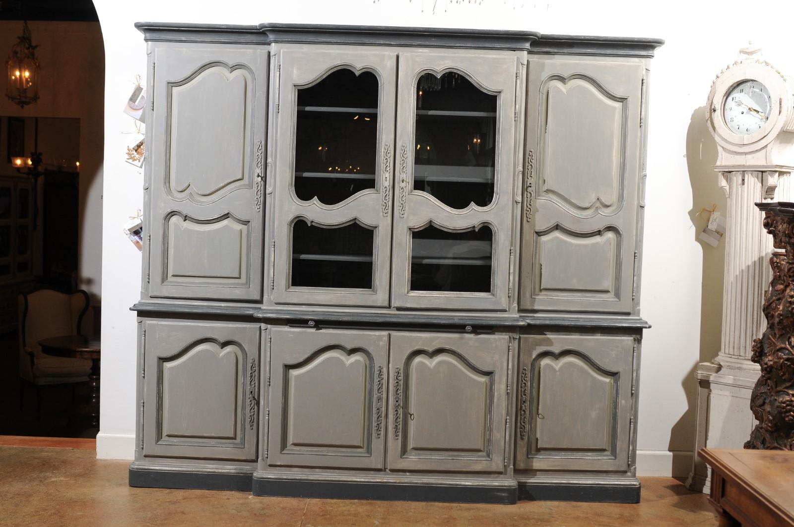 A large French vintage Louis XV style painted two-part bookcase with glass doors, custom-made for a client in 1978. This French bibliothèque features a dark grey painted cornice, sitting above a breakfront façade. The central section showcases two