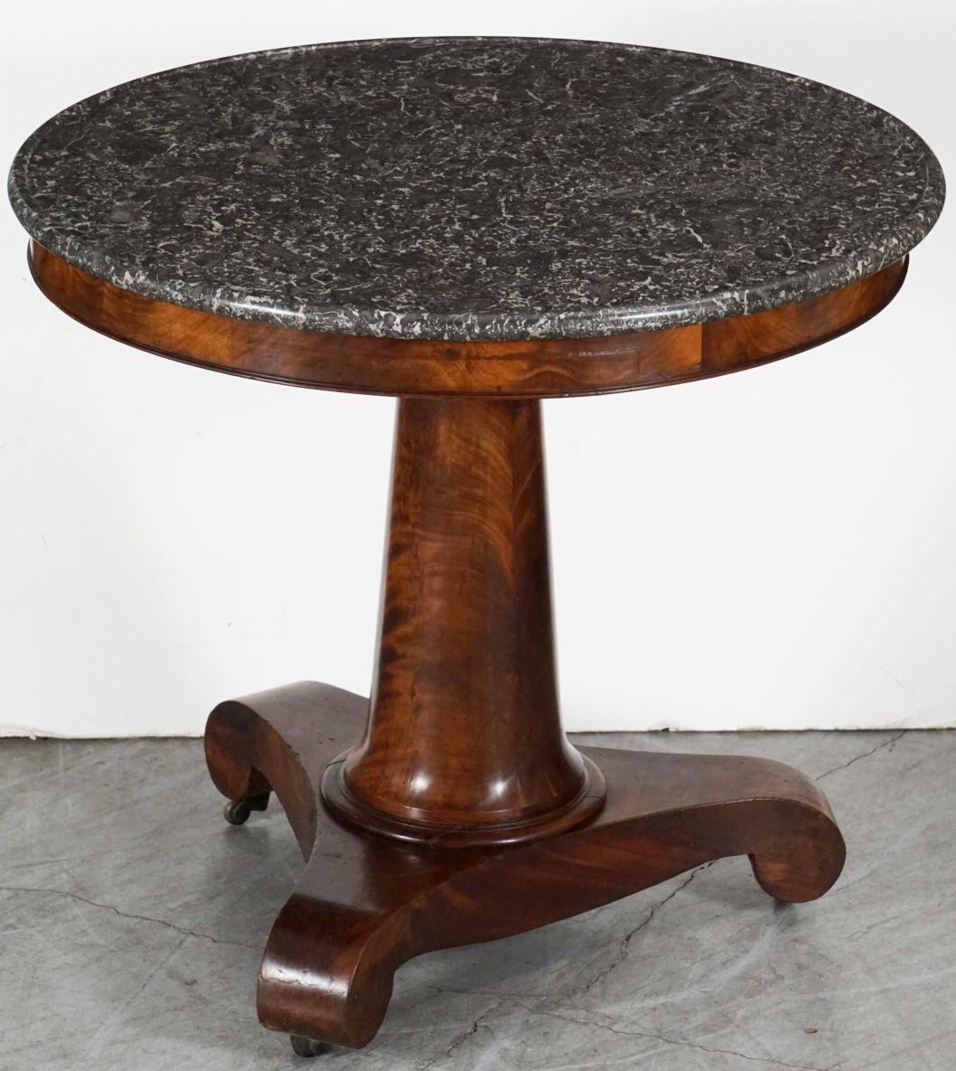 A fine French guéridon or round table from the 19th century - a beautifully figured mahogany column supporting the circular figured marble top, set upon a patinated tri-form base with scroll-form legs and resting on brass casters.