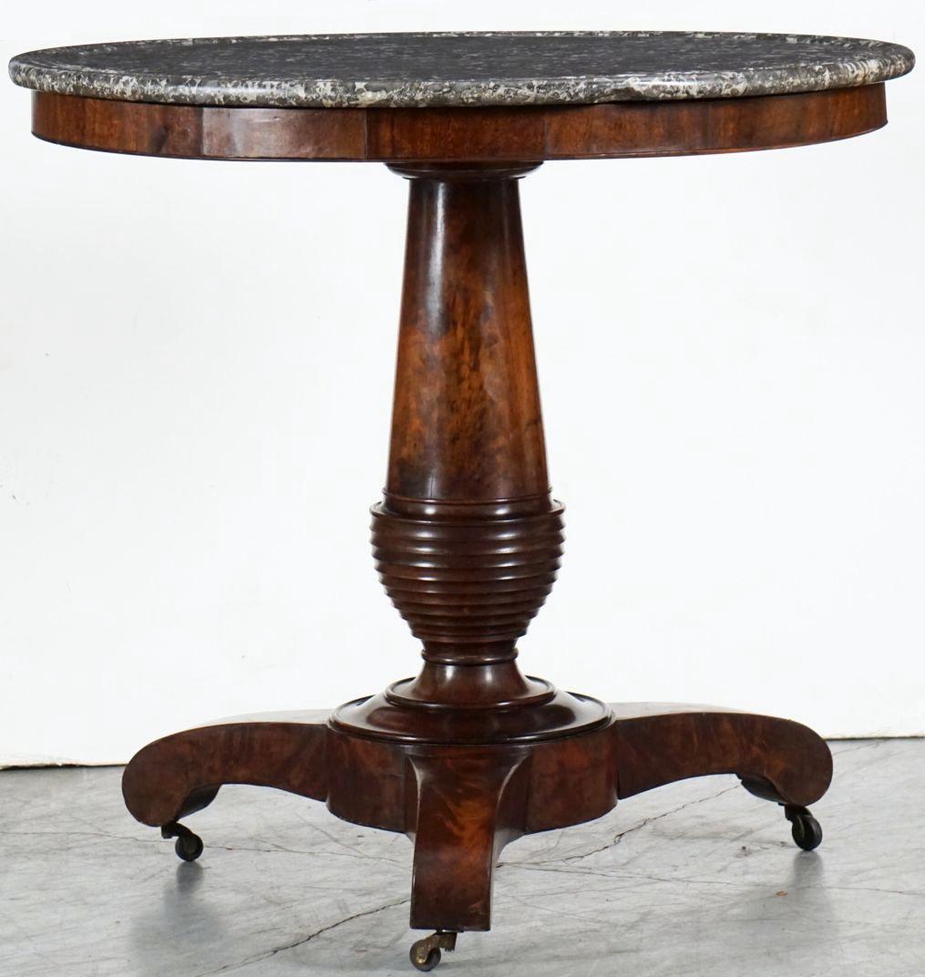 A fine French guéridon or round table from the 19th century - a beautifully figured and turned central column of flame mahogany supporting the circular figured marble top, set upon a patinated tri-form base with scroll-form legs and resting on brass