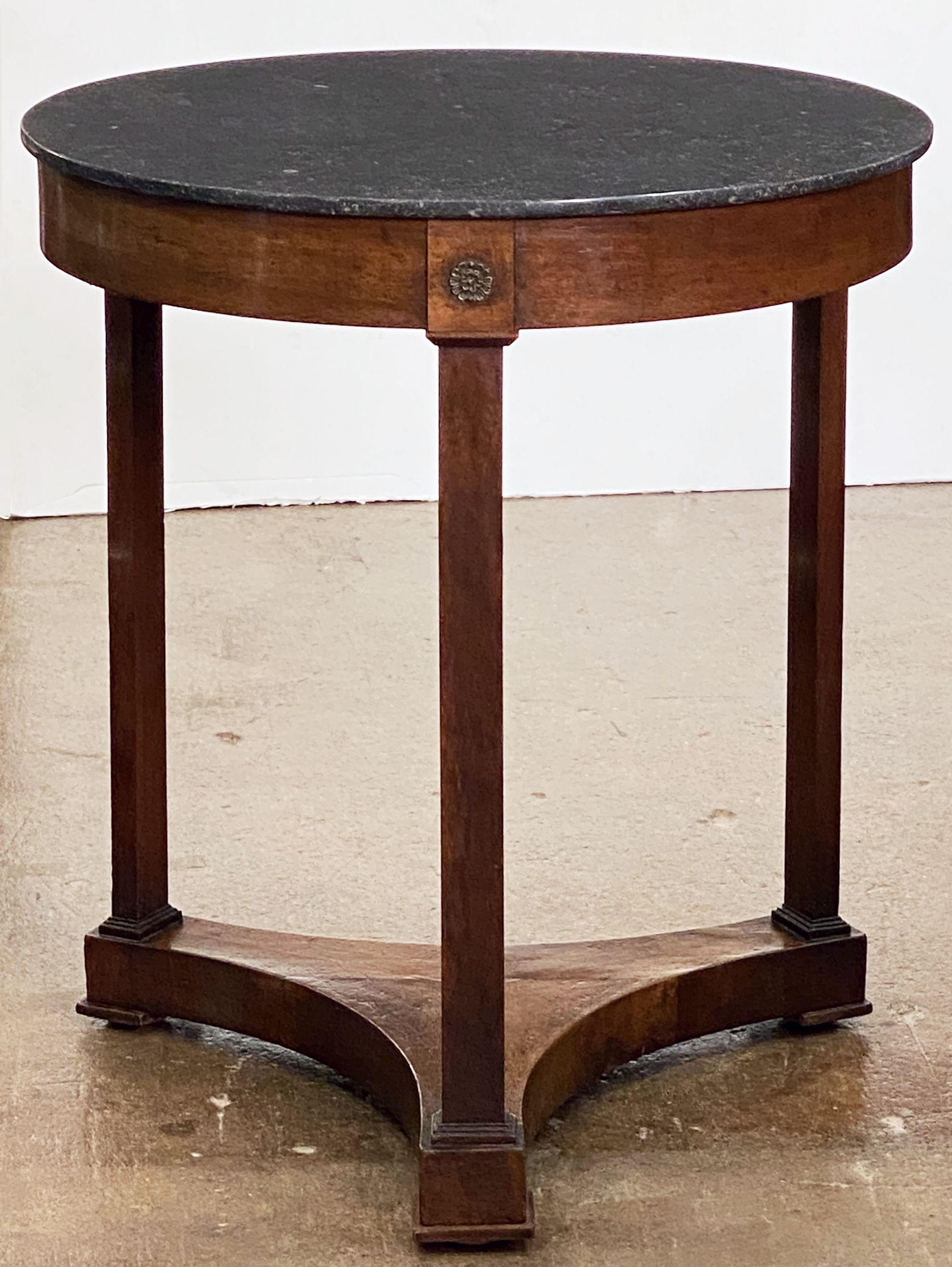 A handsome French round occasional table or guéridon in the Empire style, featuring a circular top of black marble set upon a tri-form support of mahogany with brass ormolu decorations, and resting on block feet. 

Marble top is original to the