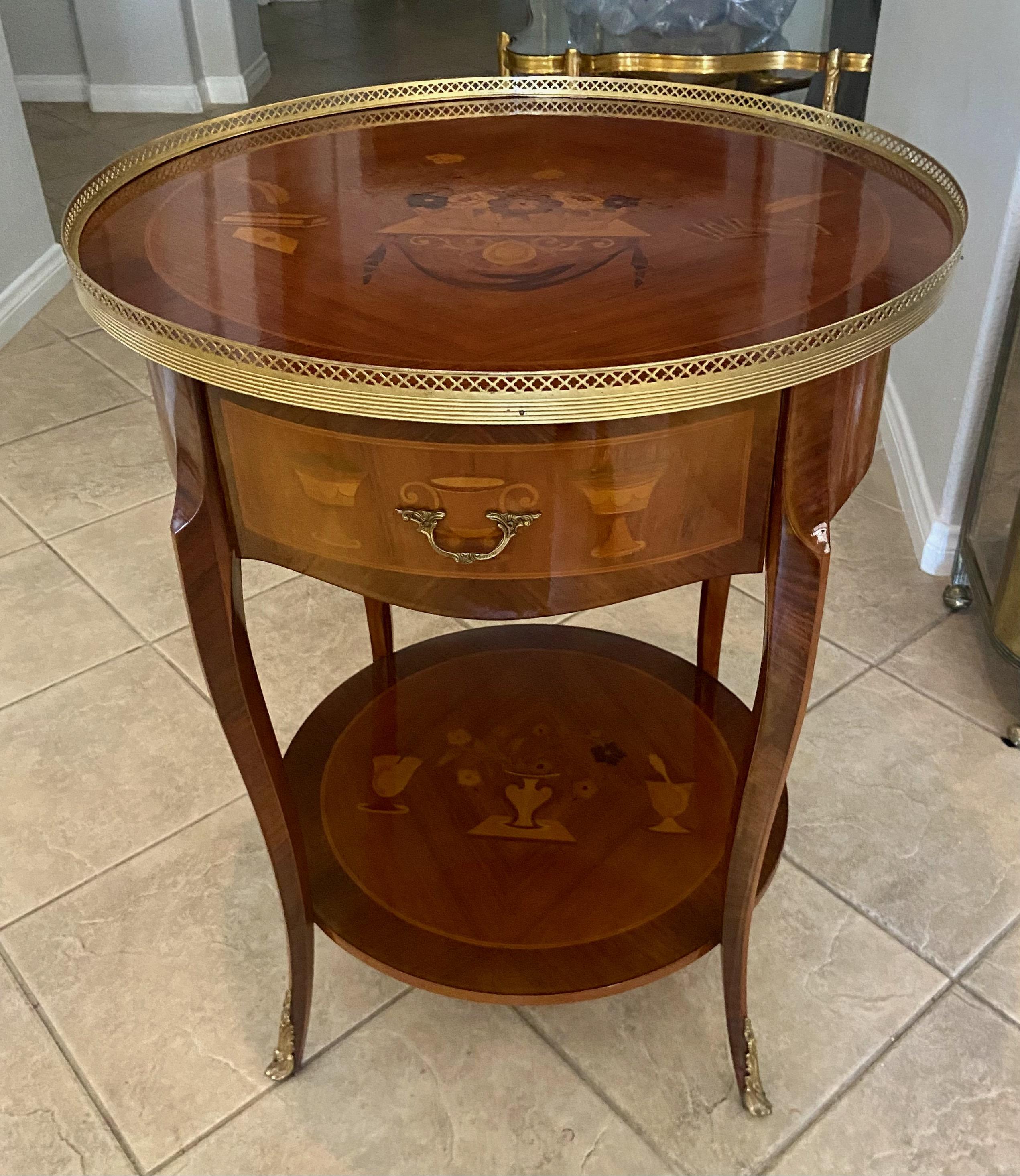 French Louis XV style 2 tier wood inlayed marquetry round side or end table. Lots of inlaid floral and urn motif throughout accentuated with brass pierced gallery rail and ormolu feet. Stamped made in Italian inside pull out drawer.