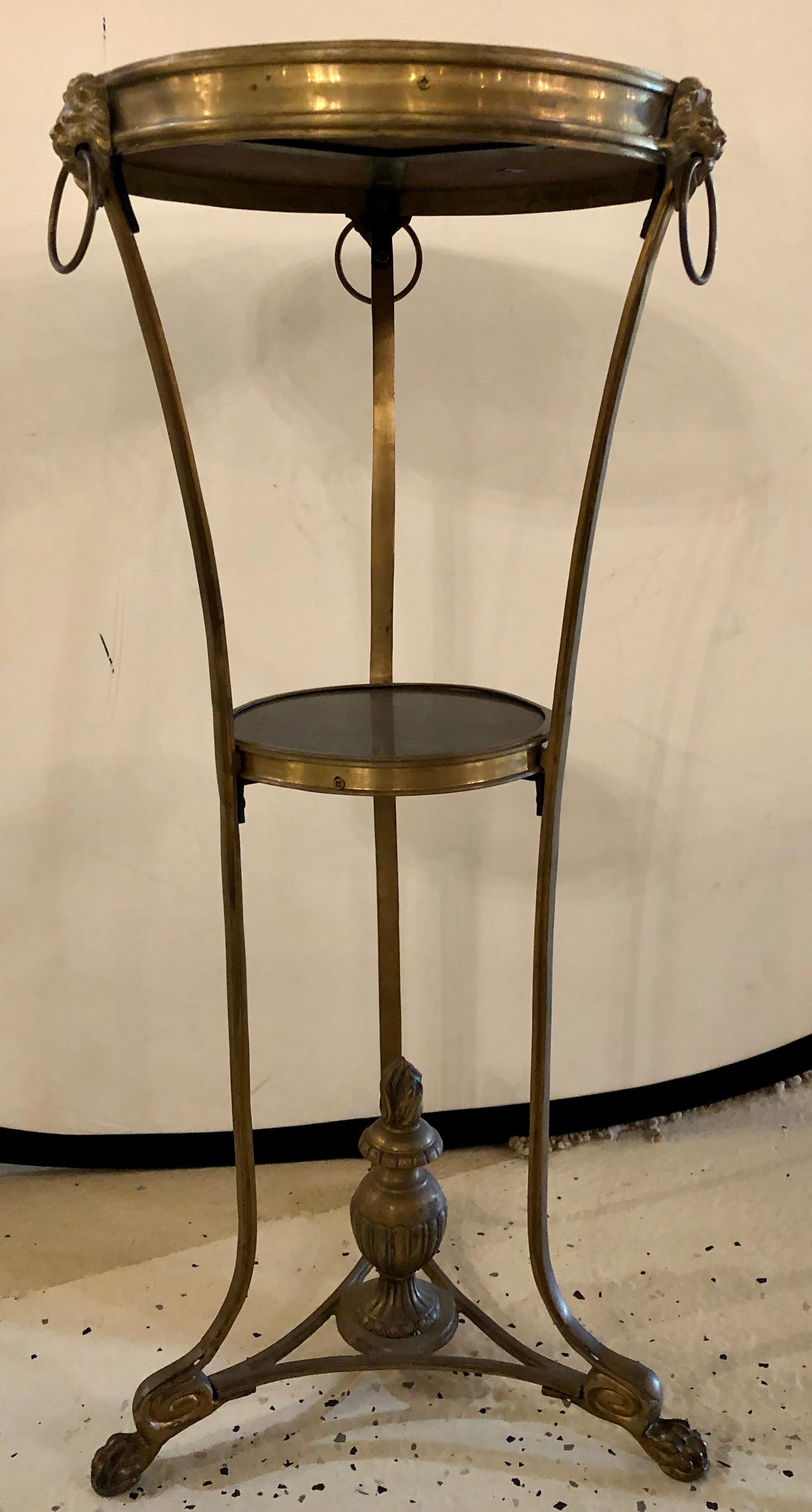 French gilt bronze and black marble round gueridon or pedestal table in the Empire taste with lion ring handles. The claw foot tri pod base having a center finial undercarriage leading to a set of curved bronze legs having a middle shelf with a