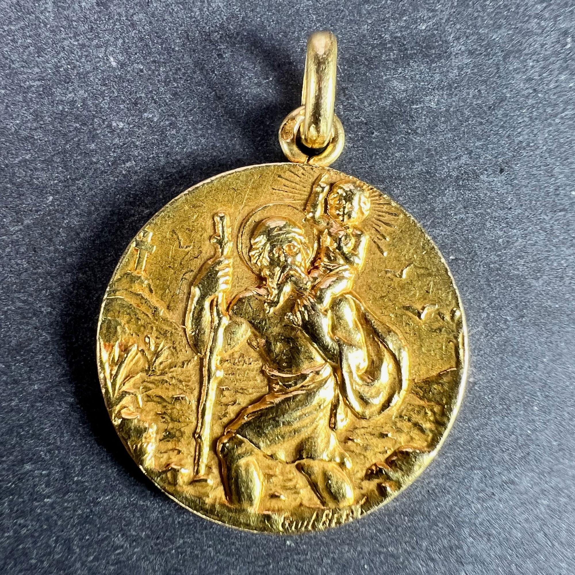 A French 18 karat (18K) yellow gold charm pendant designed as a medal depicting Saint Christopher as he carries the infant Christ across a river, the reverse with the phrase 'Regarde S Christophe Puis Va T'en Rassure' (Look at St Christopher and go