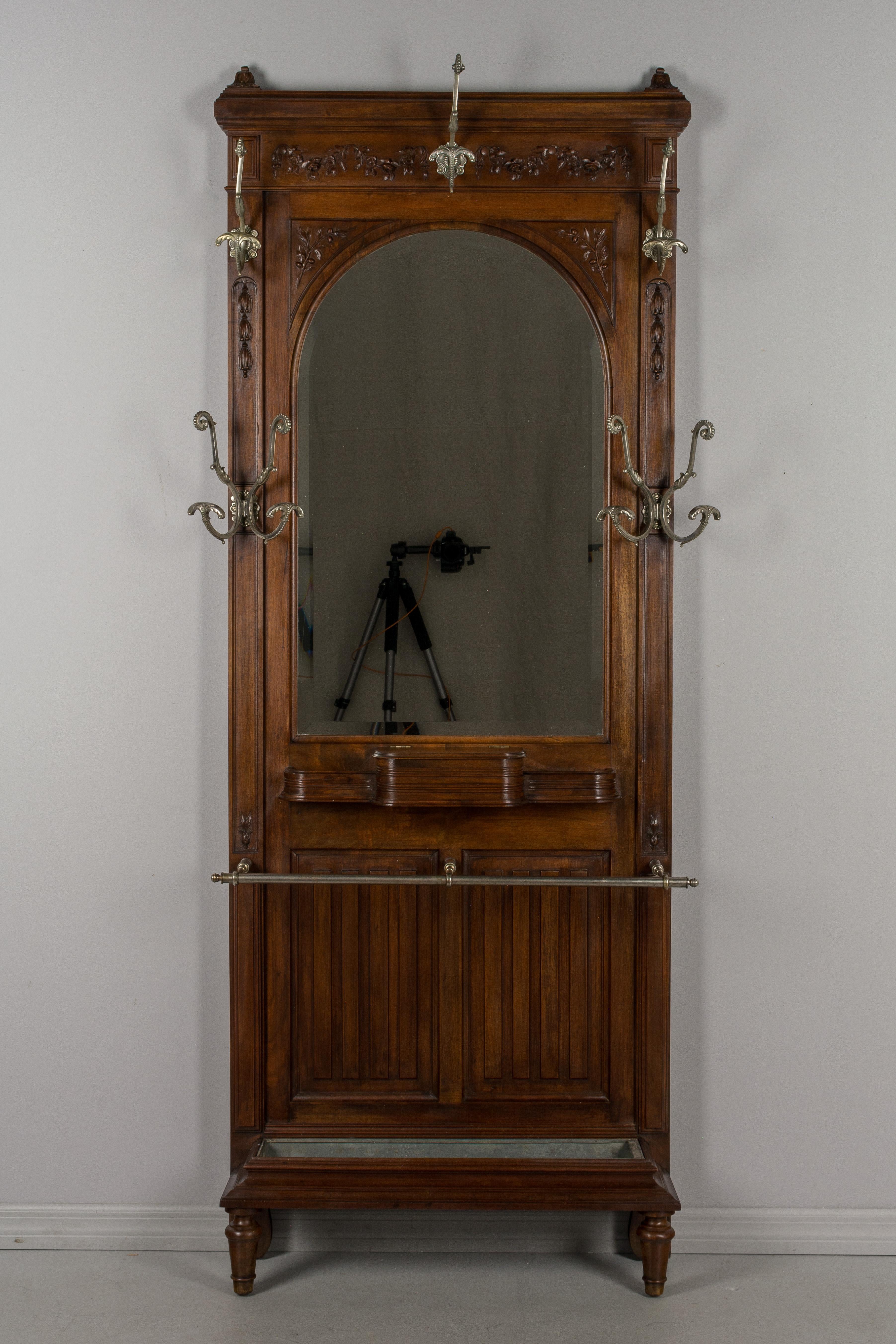 A Louis XVI style French entryway hall tree, or coat rack, with large arched beveled mirror. Made of solid walnut decorated with hand carved floral swags and olive branches. Beautifully detailed nickel plated brass coat hooks. Hinged box for gloves