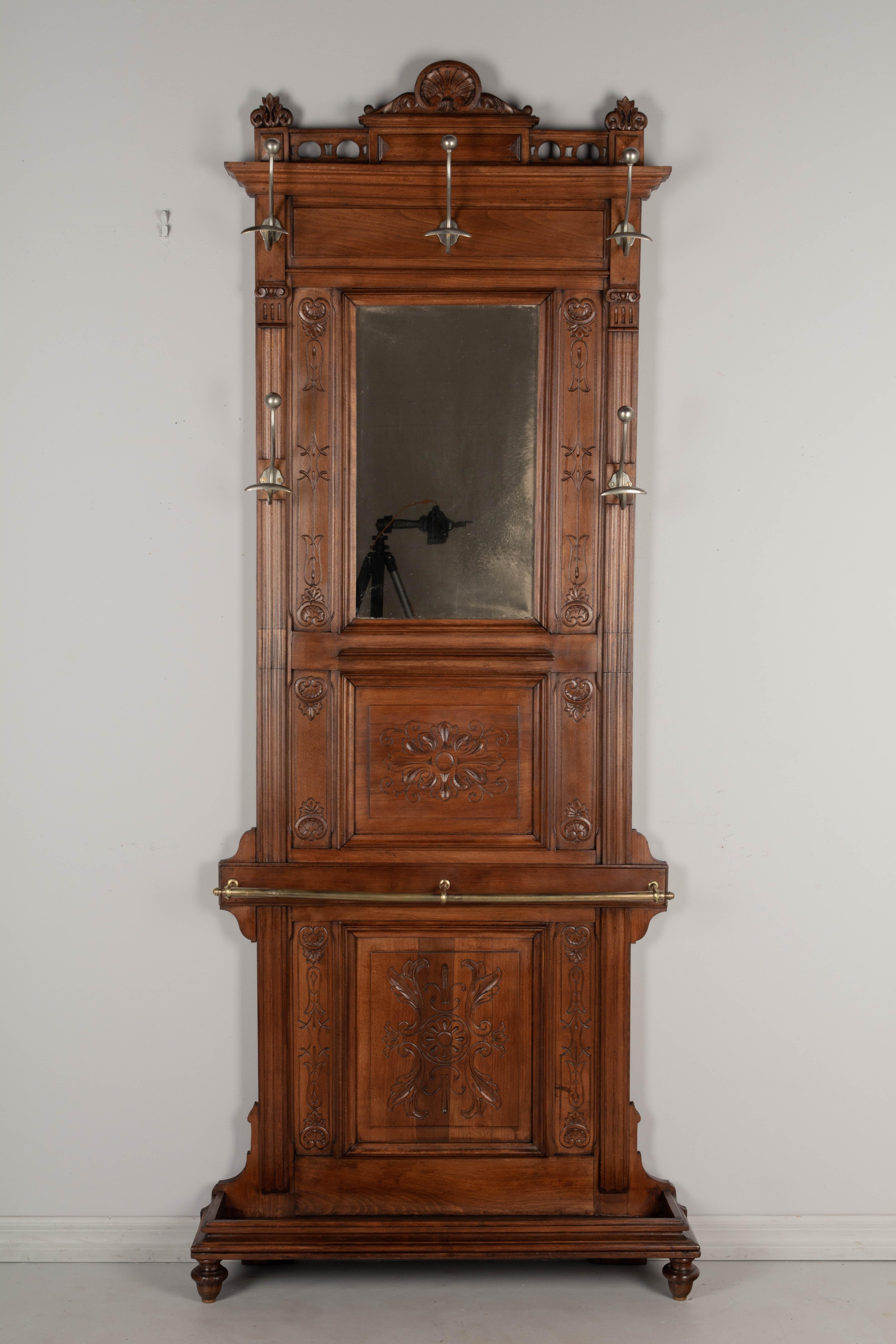 A Louis XVI style French entryway hall tree, or coat rack, with mirror. Made of solid beech wood with hand carved decoration and five coat hooks. Small shelf in the center beneath the mirror. Umbrellas or walking canes are held by a brass bar across