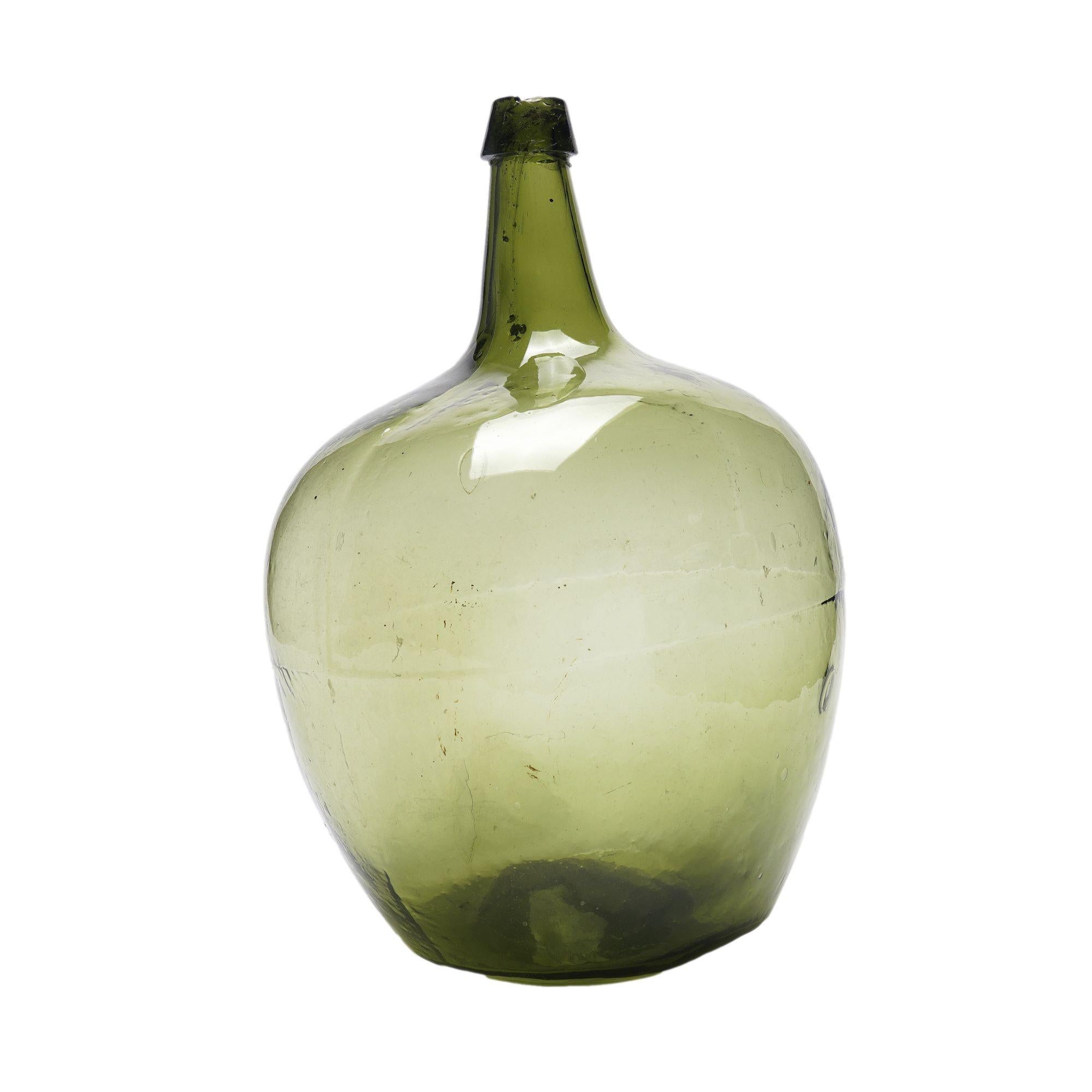 Damigiana in vetro verde oliva soffiato a mano. Le cuciture e le irregolarità sono visibili ovunque e il collo ha una leggera inclinazione.
Francia, circa 1815-35.