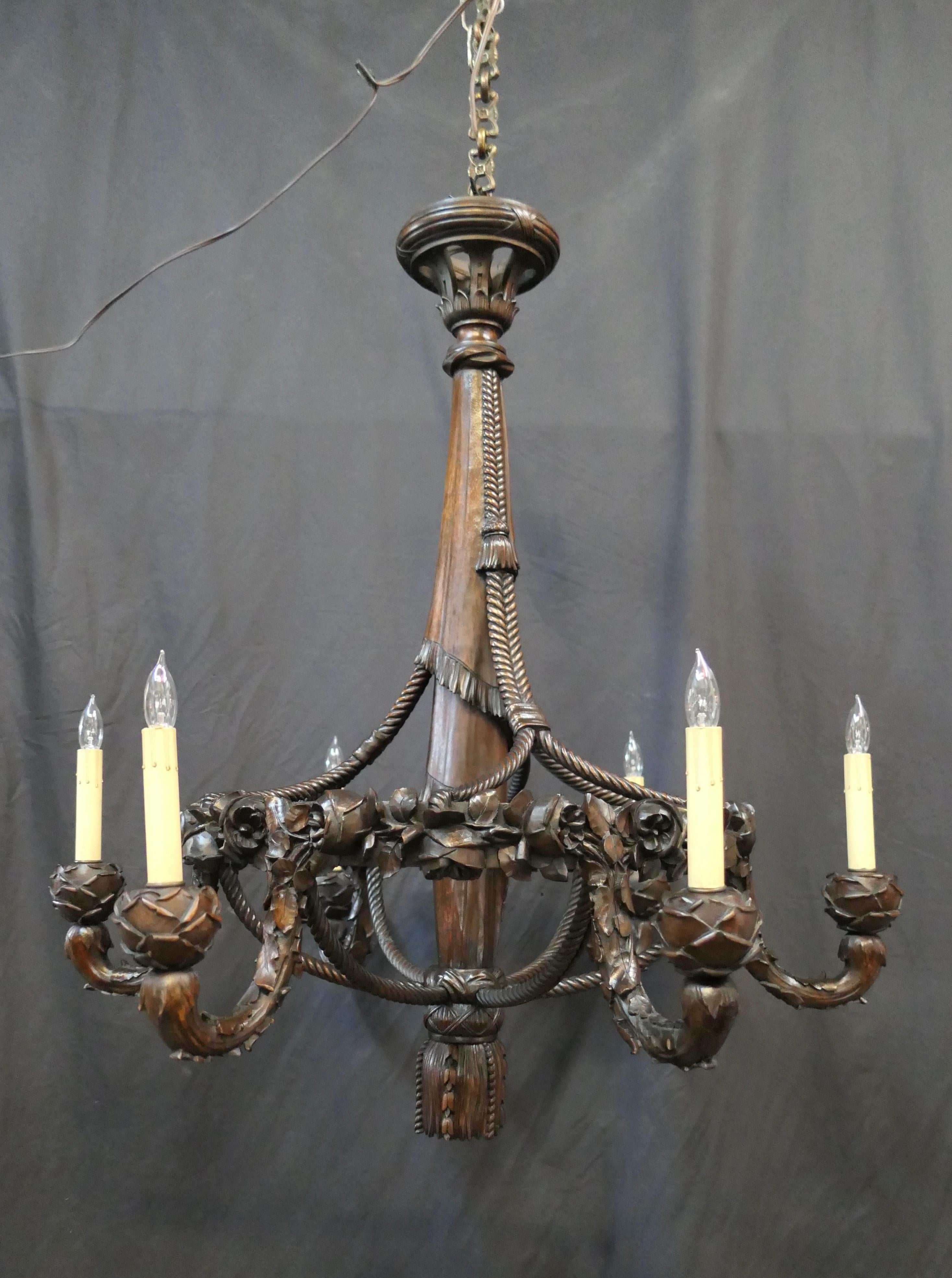 This stunning early 20th century French hand carved mahogany wood formal chandelier is exceptionally designed with six curved arms embellished with a carved leaf motif. Each arm holds a bulbous bloom supporting a tall cream color candle sleeve with