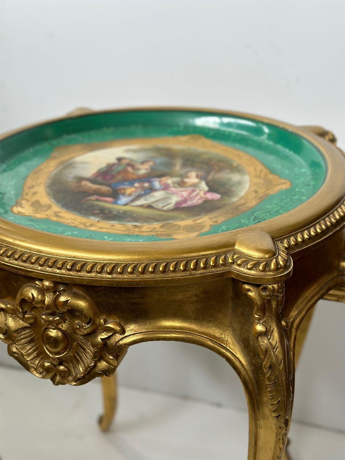 Hand-carved wood table with porcelain plaque and gold finish depicting a small group in a garden accompanied with a lamb. Made in France, circa 1900s. 

Dimensions:
31.25