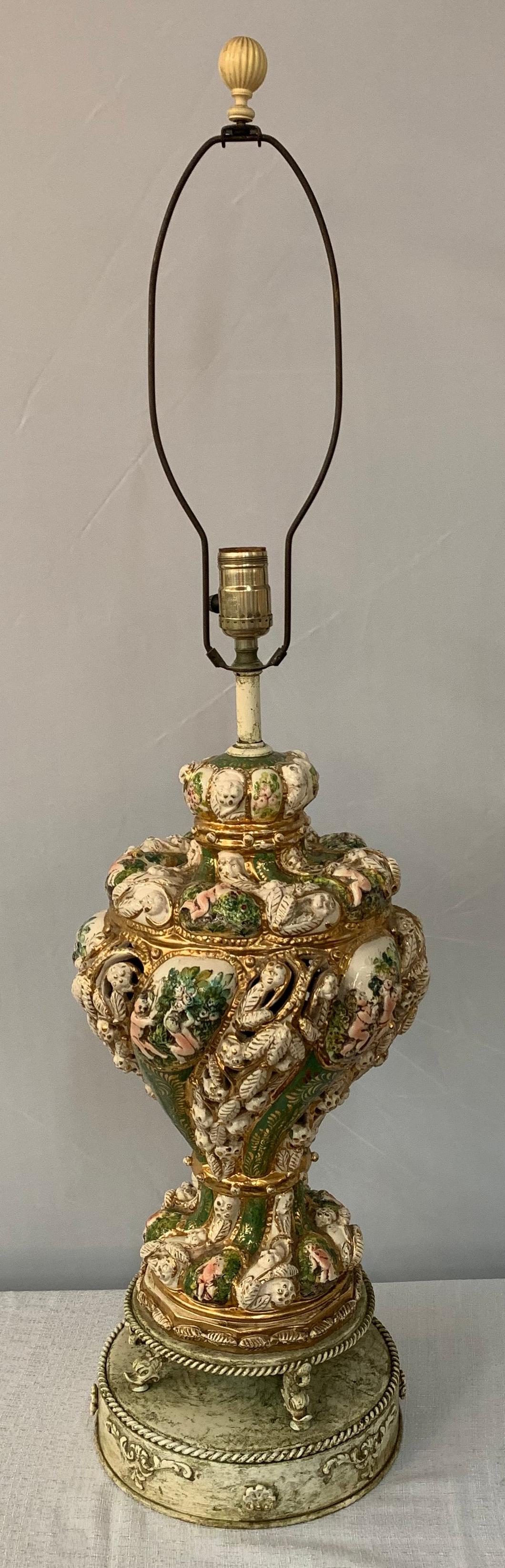 An exquisite French Dresden style hand painted porcelain table lamp featuring incredible details in green, white, pink and gold. The base lamp depicts floral design and figures of what is looks like wingless putti in a tasseled shape elevated with a
