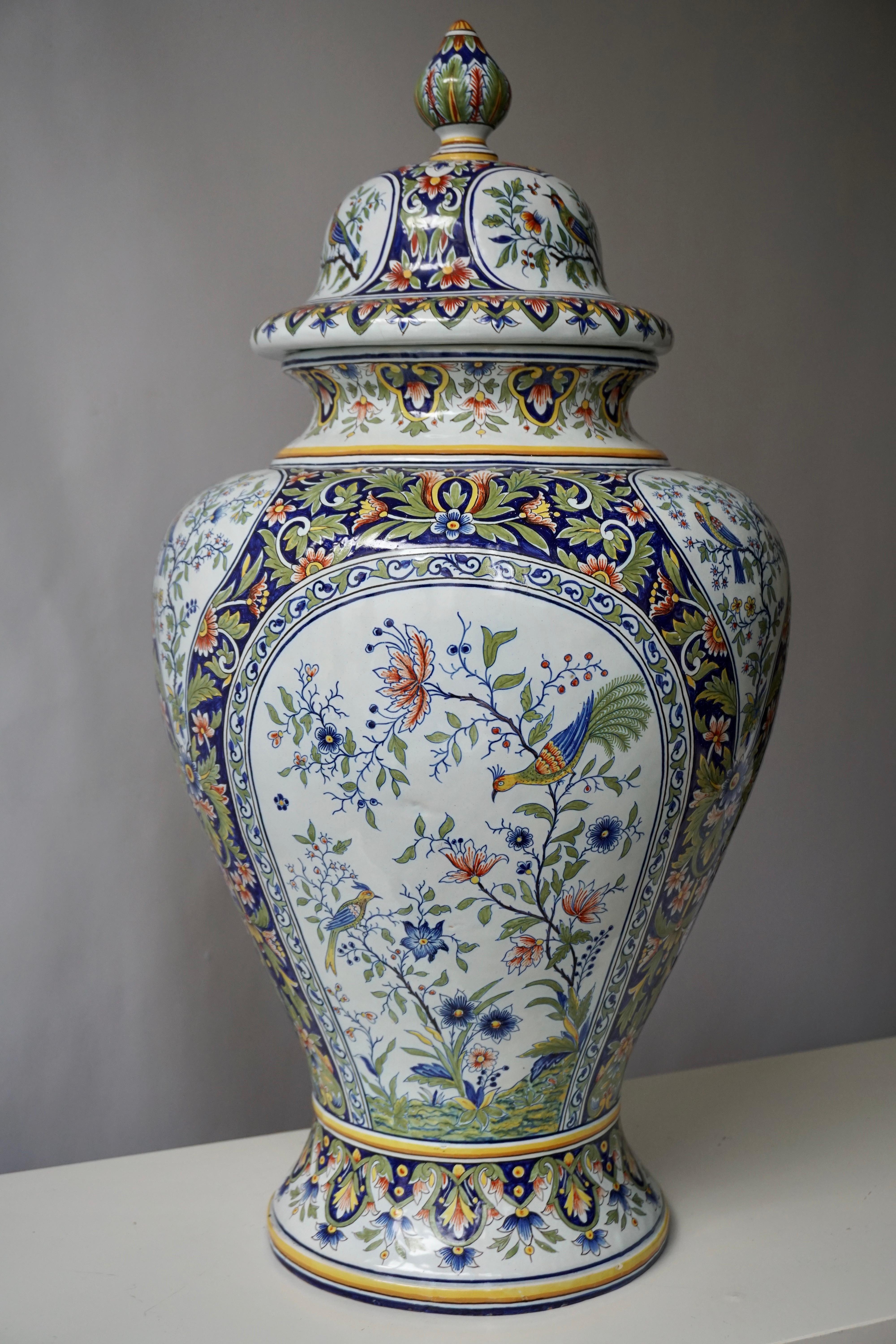 This elegant vase was crafted in Normandy, circa 1950. The ceramic, rounded potiche features hand painted flower decor with birds in a traditional blue, white, green and yellow palette. The lid of the porcelain vase is topped with three small bird