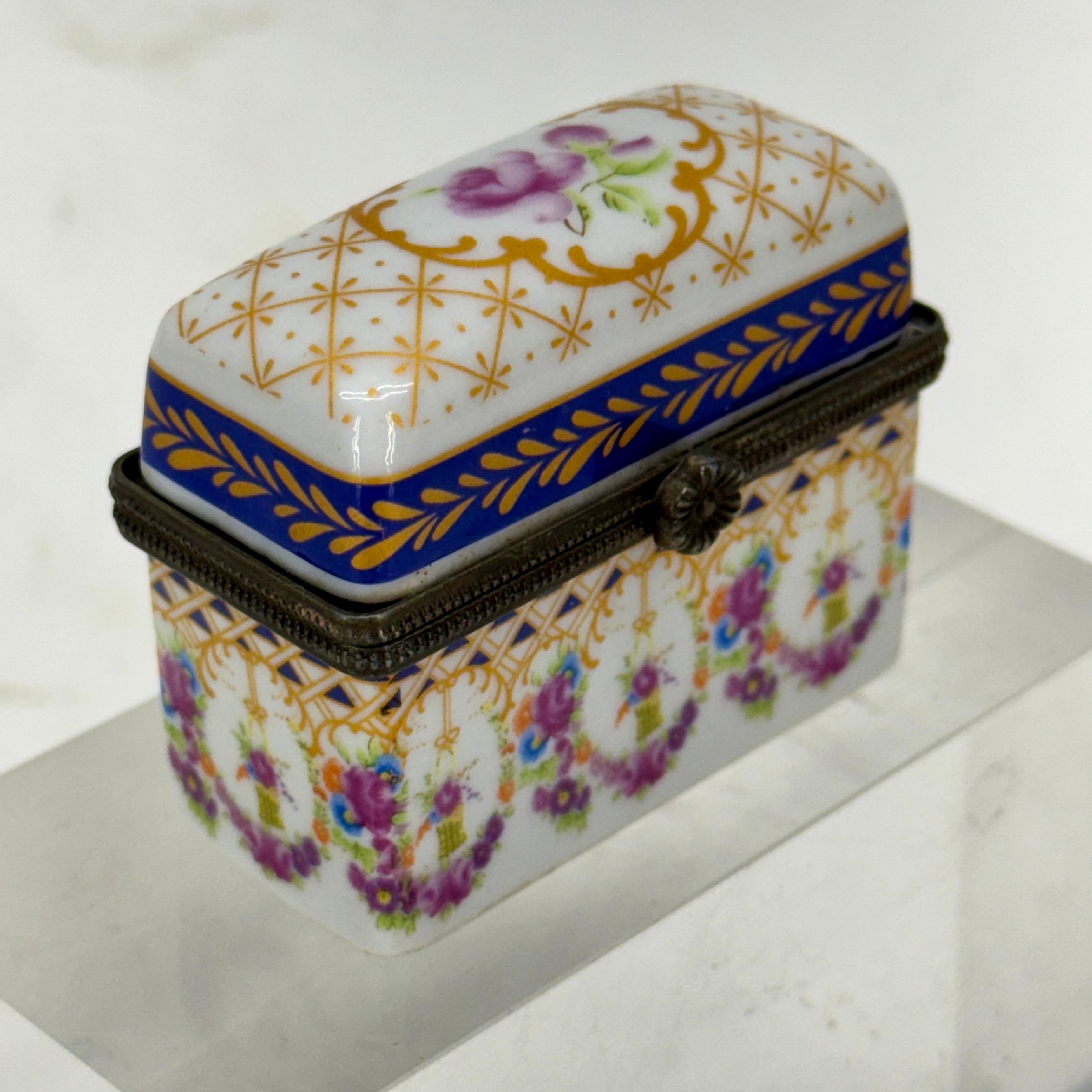 Encantadora caja de baratijas de porcelana pintada en morado, dorado, verde y azul real. Al abrir la caja hay un bonito diseño floral dentro de la tapa. Esta pieza sería sin duda una fantástica adición a una colección existente de estas deseables