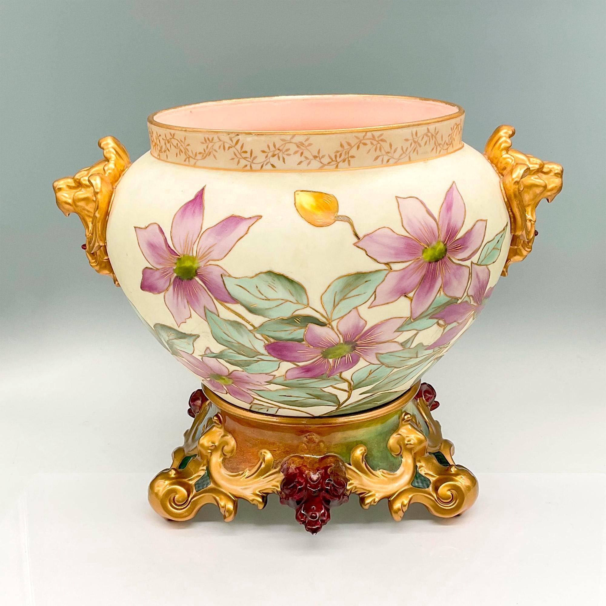 Introducing a stunning Mid 20th Century French Limoges porcelain jardiniere and base set. This exquisite ensemble showcases matte porcelain decorated with hand-painted flowers in shades of purple, white, and yellow, complemented by lush green