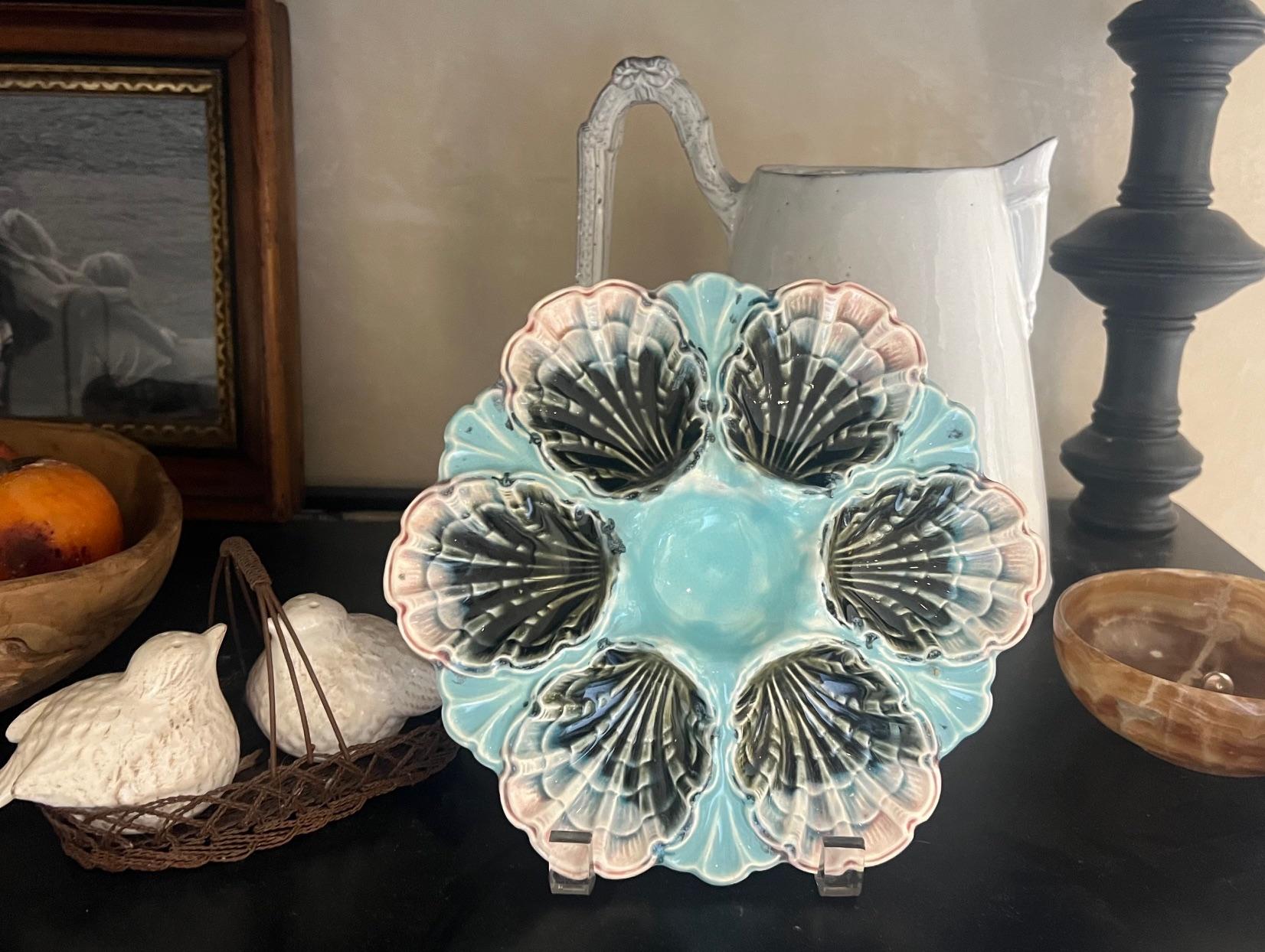 A French majolica oyster plate made by Fives Lille, at the end of the 19th century. The plate has a raised central sauce well surrounded by six scallop edged wells. The colors on the shells start black and turn to blue and then pink. Marked on the