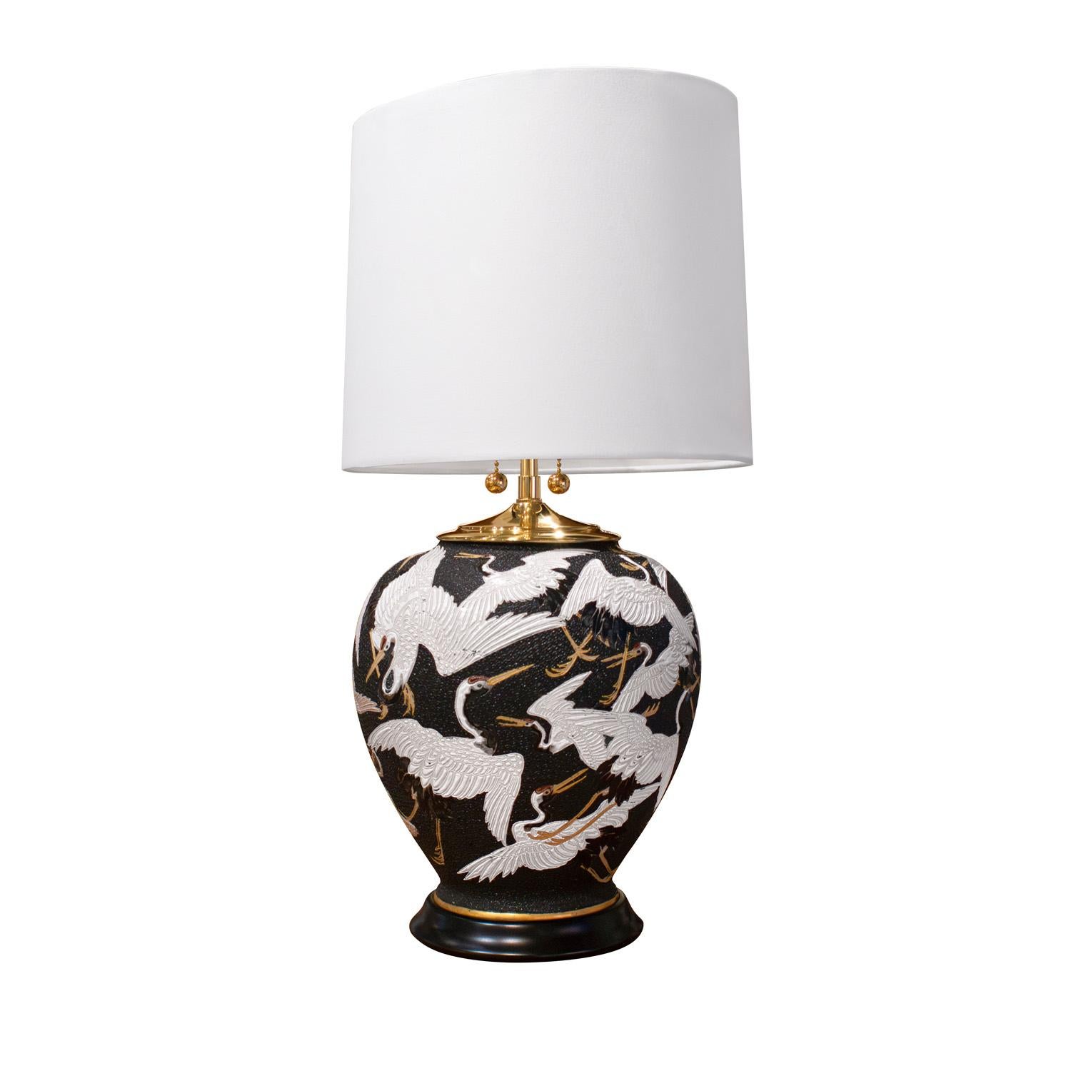 Magnifique lampe de table en porcelaine avec des grues volantes, peinte à la main avec une base ébonisée et des accents en laiton poli, France 1950's. Cette lampe est incroyablement chic. Le métal a été professionnellement nettoyé et poli. Le