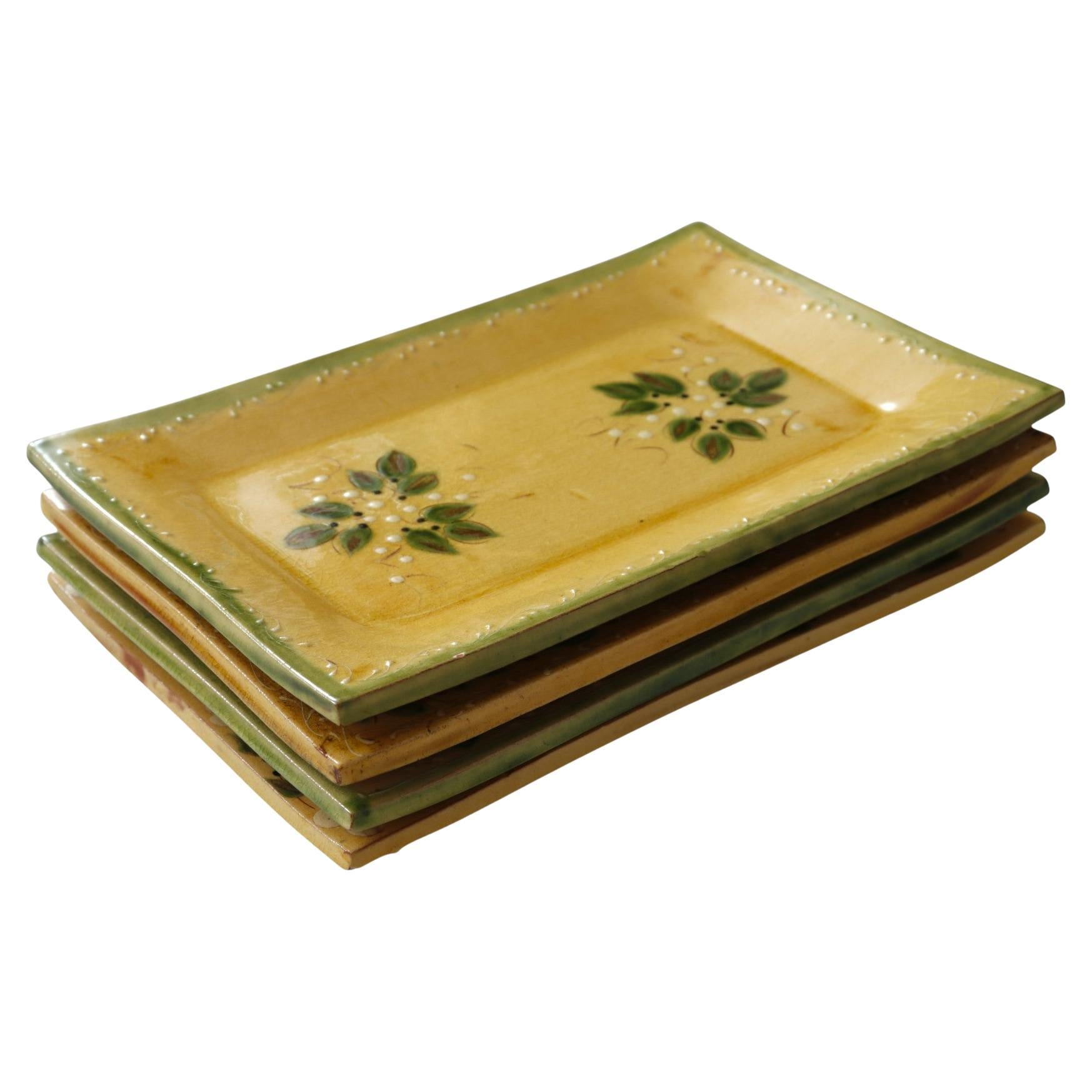 A set of four rectangular hand-painted terracotta tile serving plates, made in France. Intricate leaf and vine details decorate the plates in green with red and white, over a yellow base. Marked ‘Made in France’ underneath. Dimensions per plate.