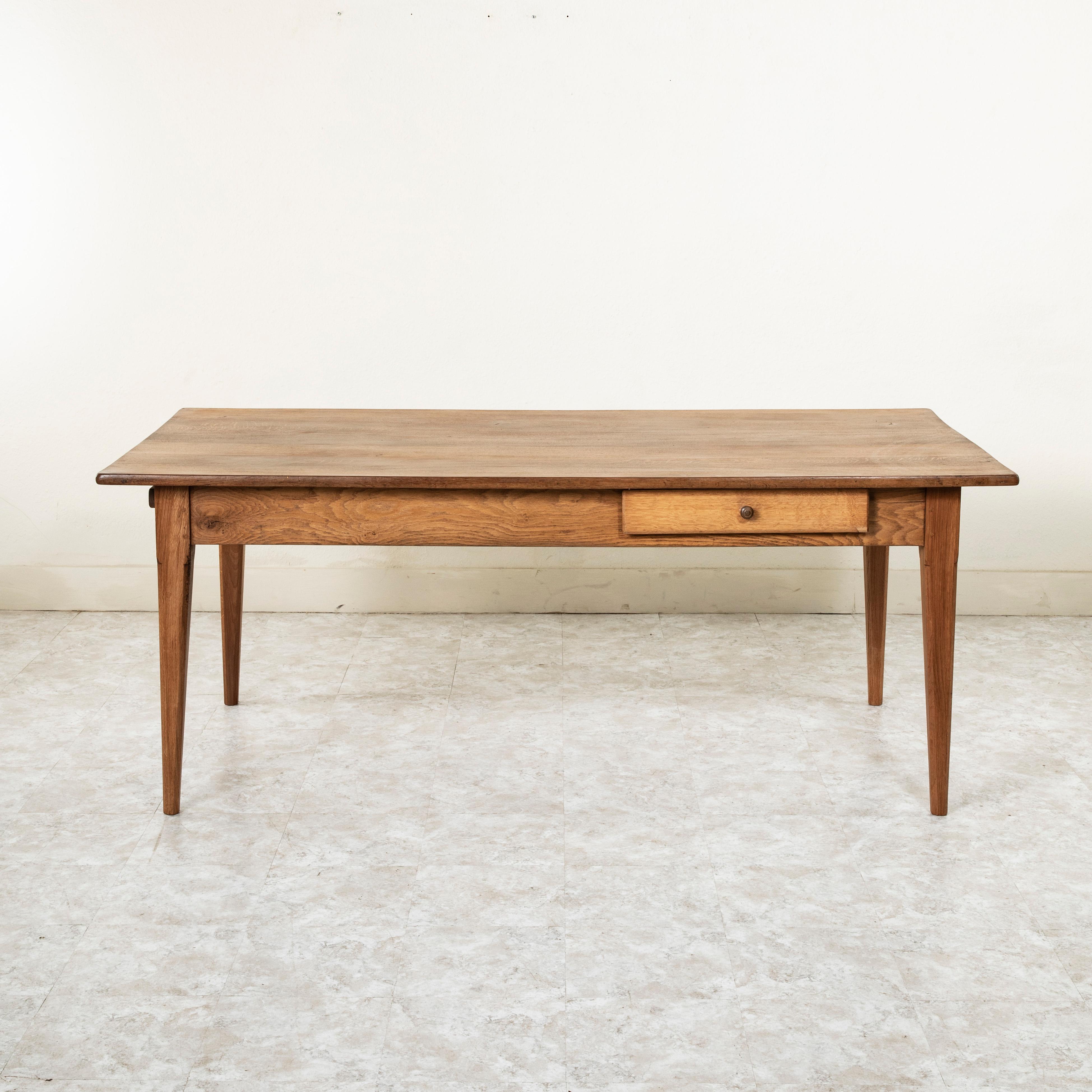 This artisan made farm table from the turn of the 20th century is from the region of Le Perche, a sub-region of Normandy, France. Its oak top measures 78 inches long and 39 inches wide. Resting on a hand pegged oak base of mortise and tenon joinery