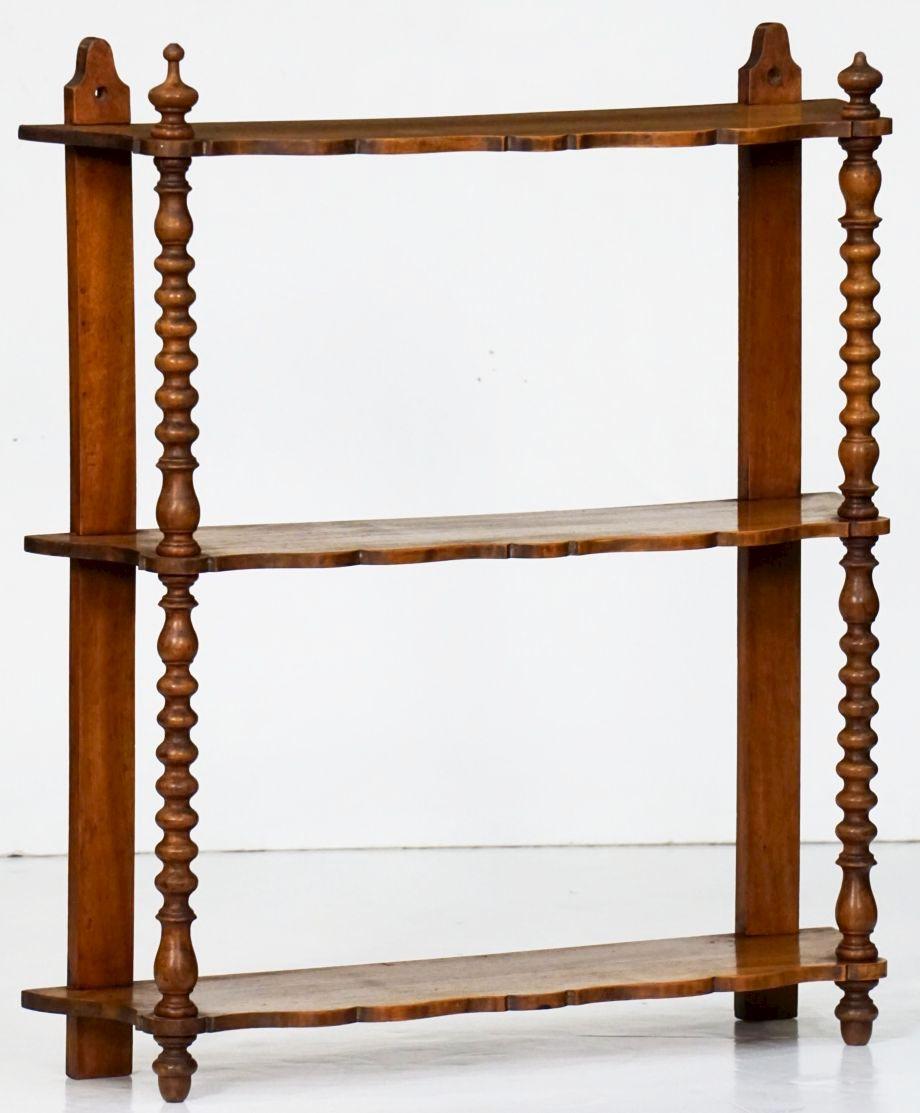 A fine French hanging curio shelf of walnut featuring three serpentine shelves adjoined by turned wood supports, with decorative finials above the top shelf.