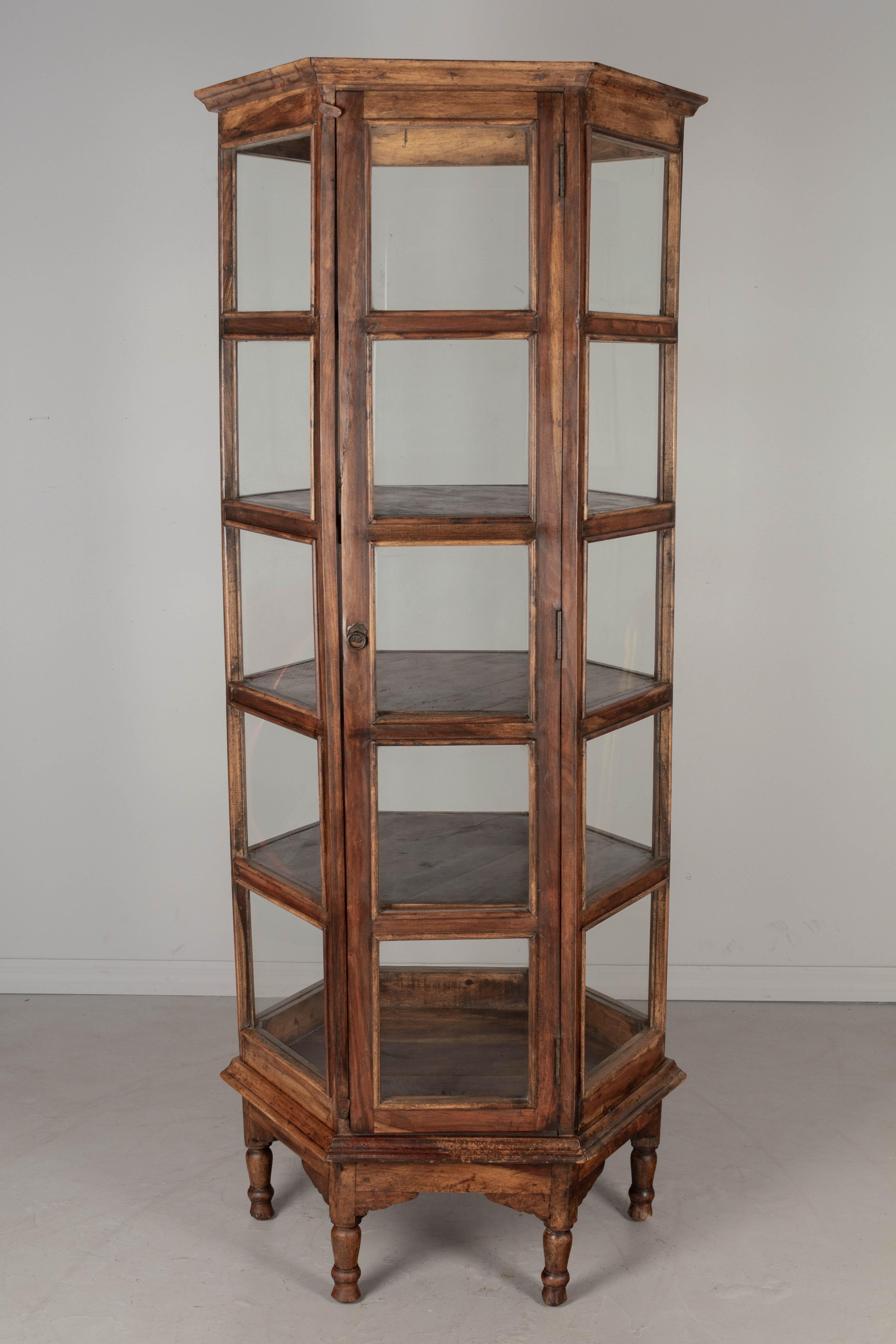A large, heavy hexagonal glass paned vitrine, or display cabinet, with four shelves. Hand-crafted hardwood frame with tuned legs. Door with ring pull and wooden latches at the top and bottom. Circa 1950s.
Overall dimensions: 78.25